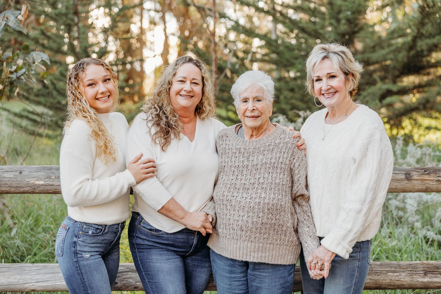 Four generations of family members in coordinated outfits smile together outdoors.