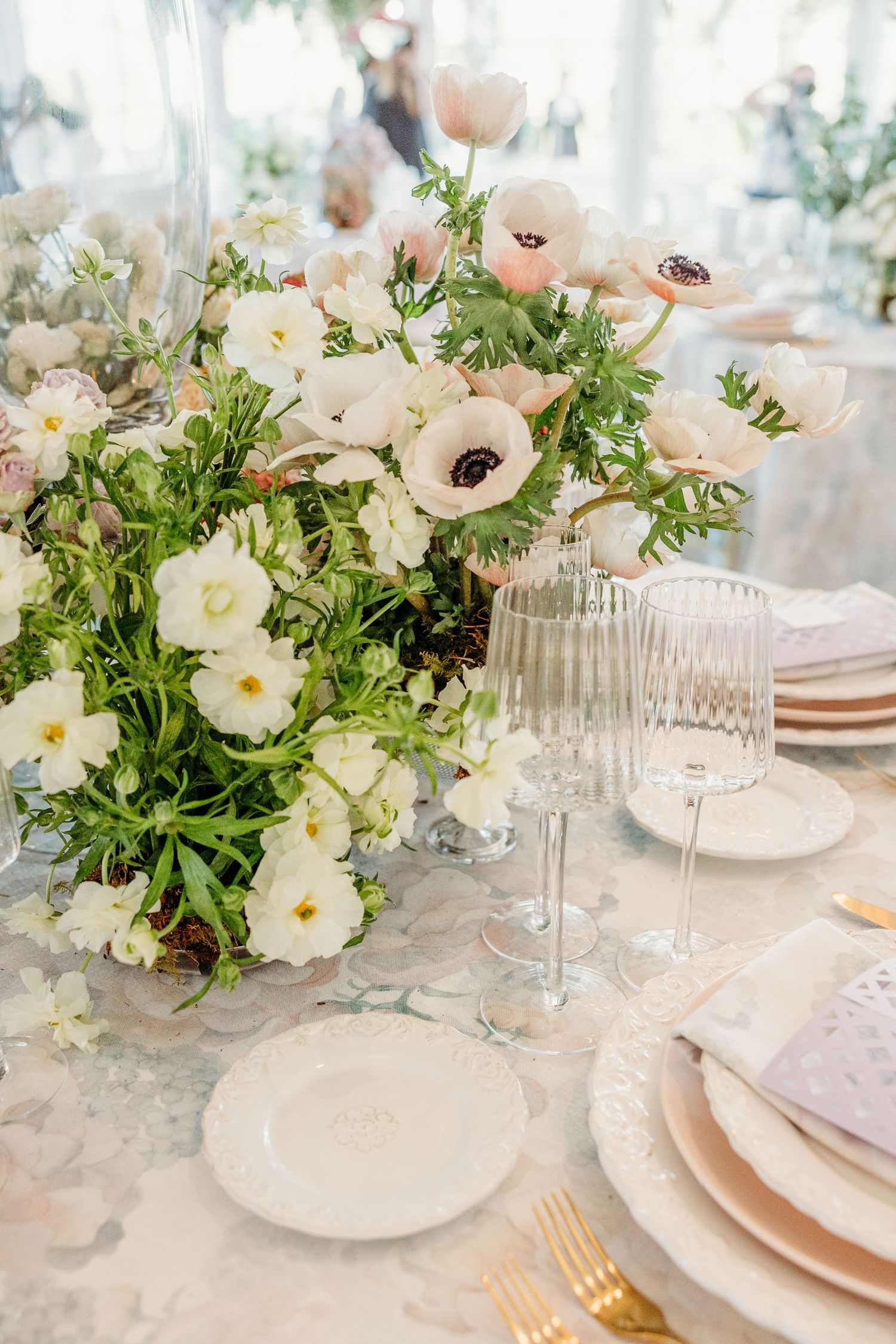 Elegant wedding table setting with white floral centerpieces, blush pink plates, and crystal glassware on a light tablecloth.
