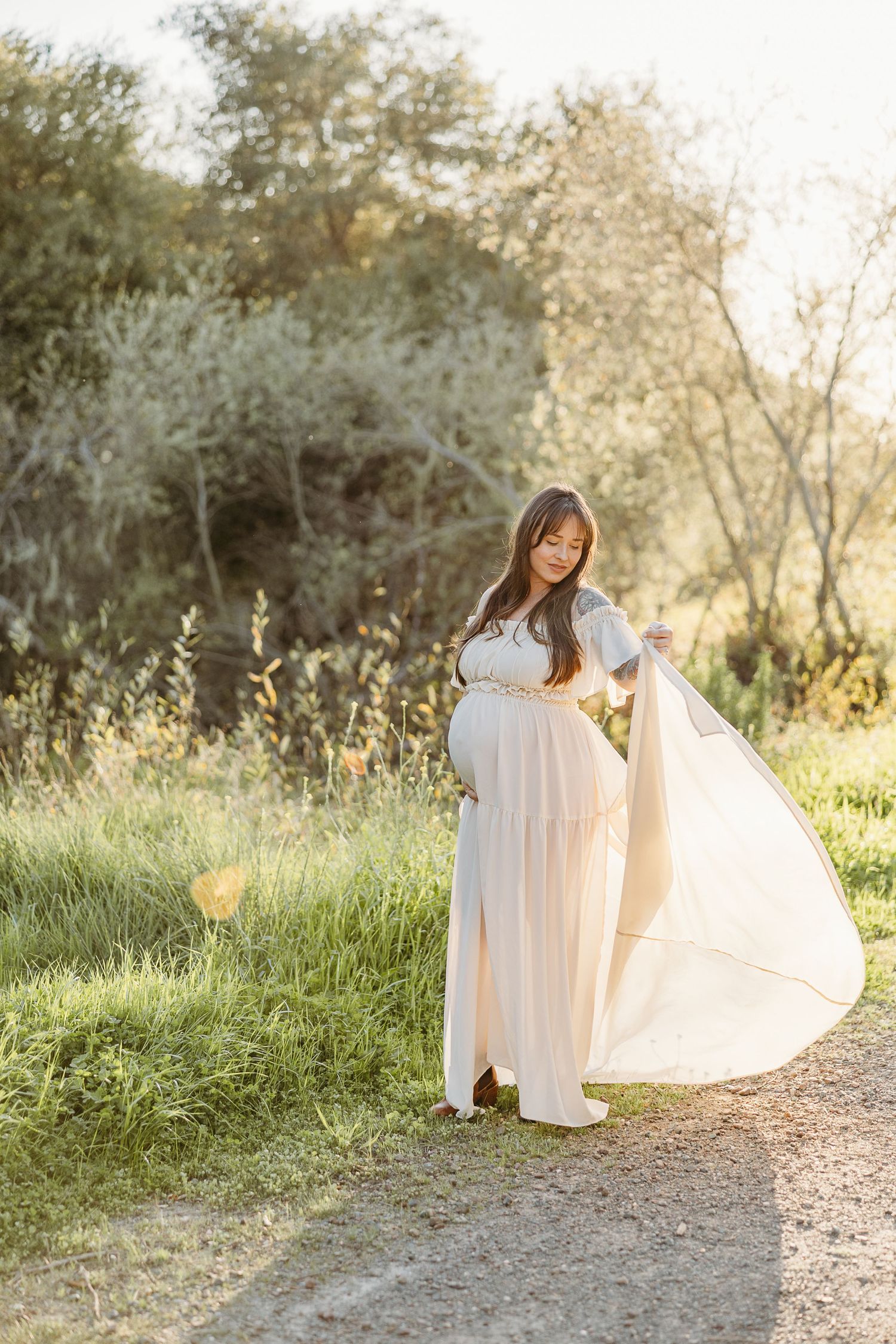 Person in flowing white dress twirling on nature path during golden hour.
