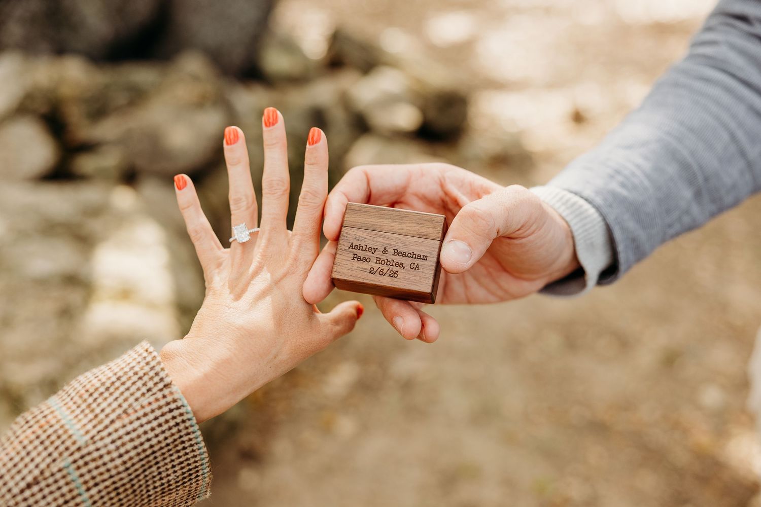 A hand wearing a beige sweater reaches for a small wooden box held by another person in a gray sleeve.