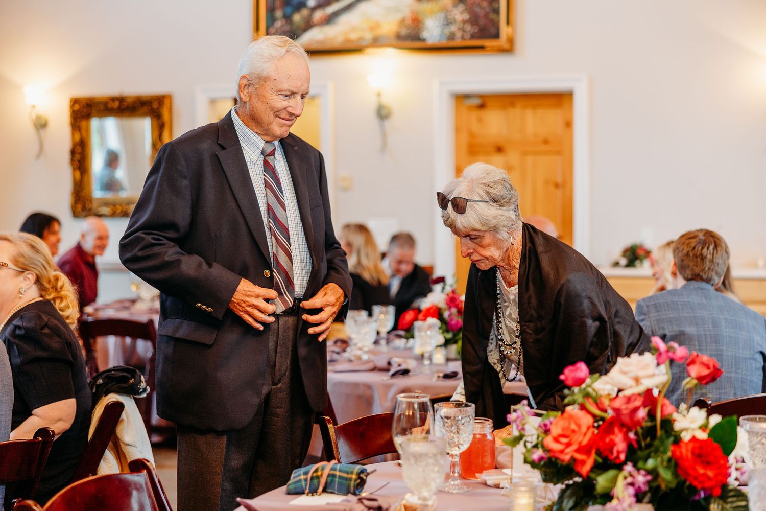 Wedding reception hall with guests seated at decorated tables and warm lighting.