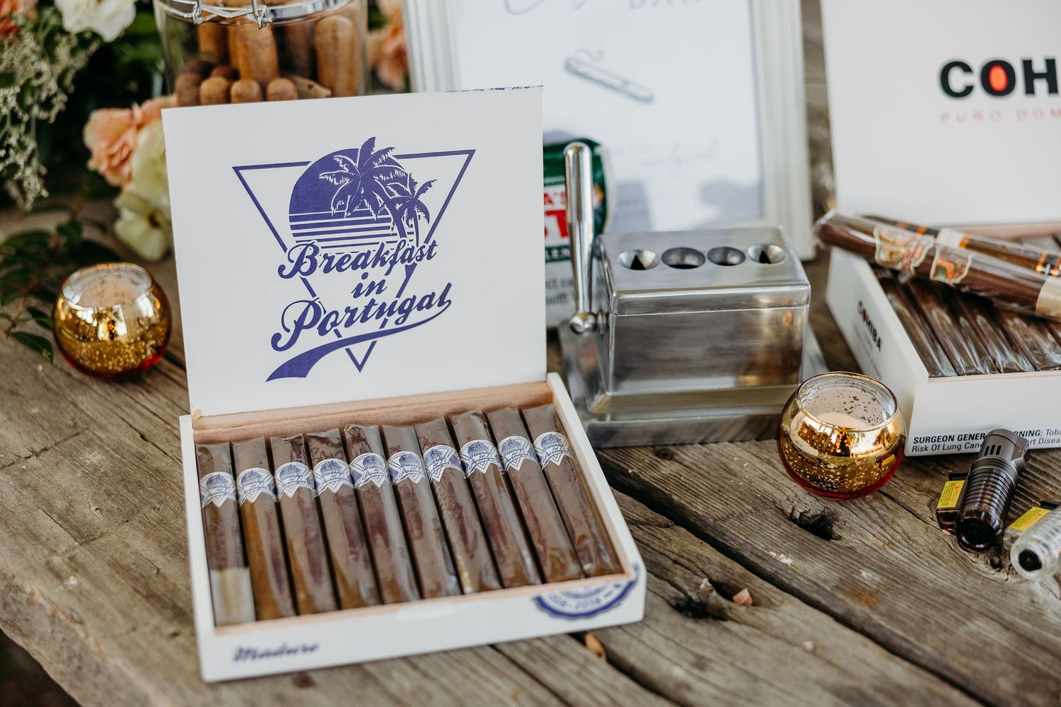 Vintage cigar boxes and smoking accessories arranged on wooden table at wedding reception.