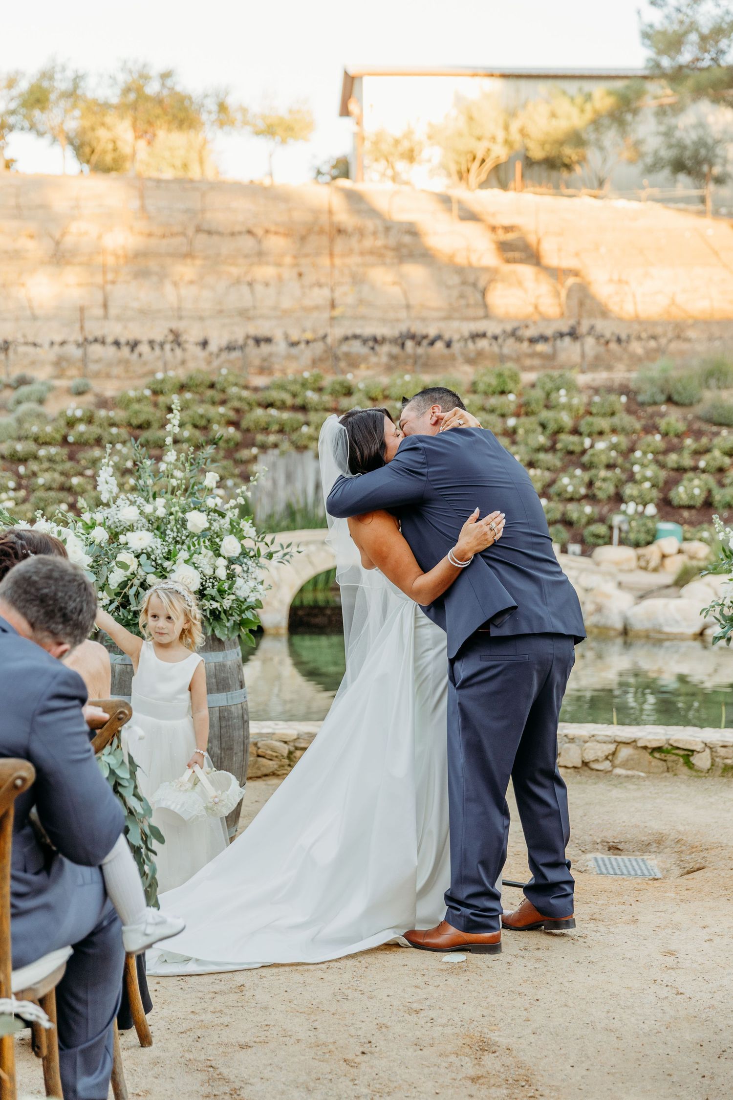 Photographer capturing candid moments at an outdoor wedding venue with stone walls and greenery.