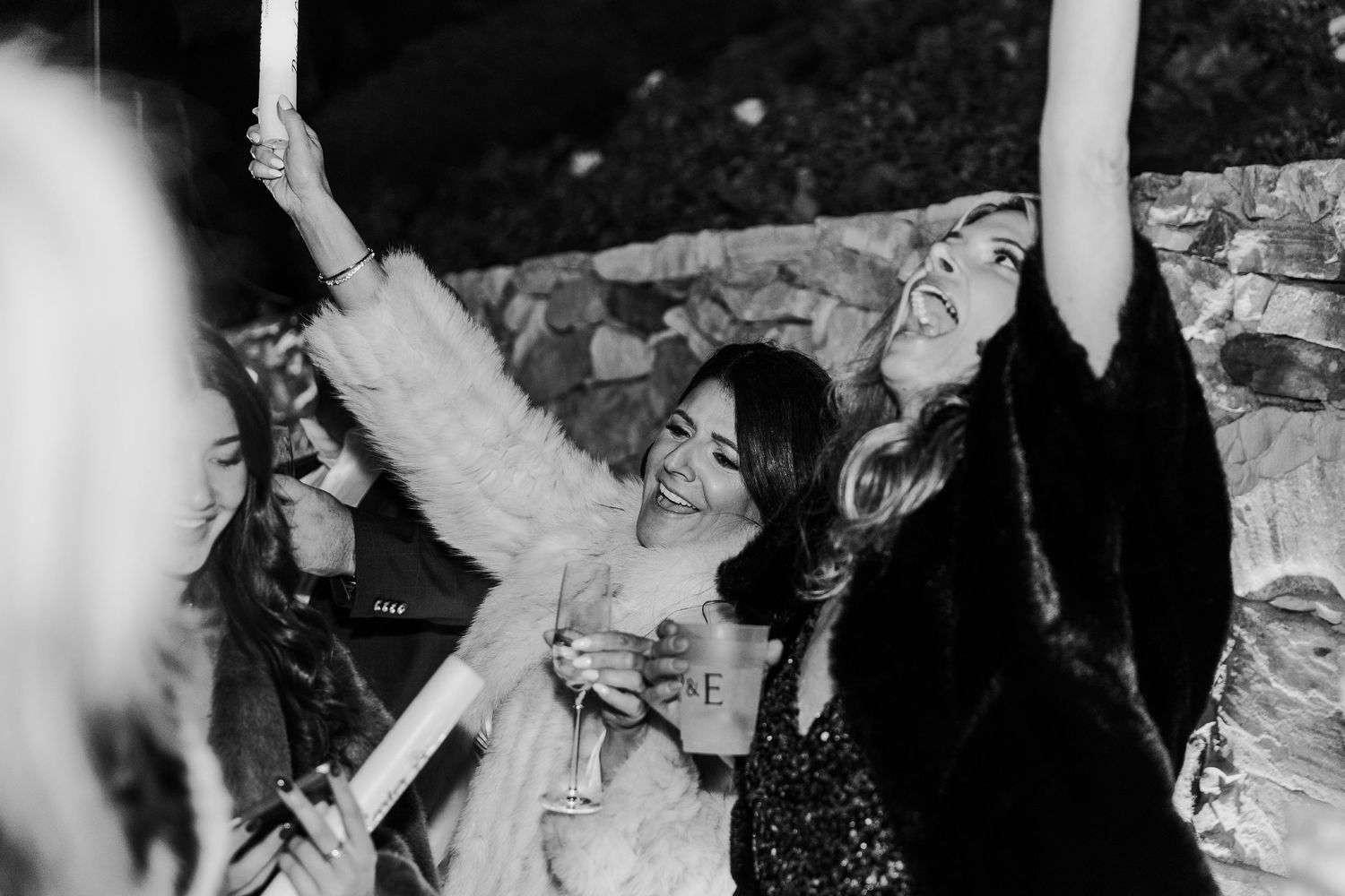 A black and white photo capturing the joyful energy of people dancing with raised arms.