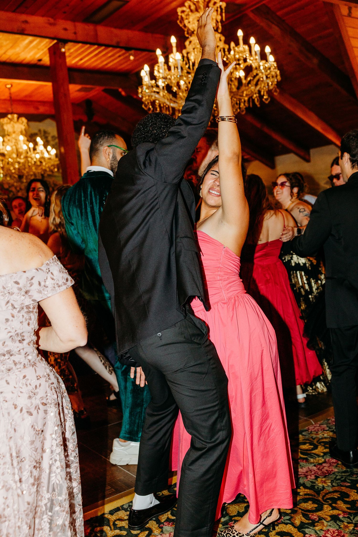 Wedding reception dance floor with guests dancing under elegant chandeliers in warm lighting.