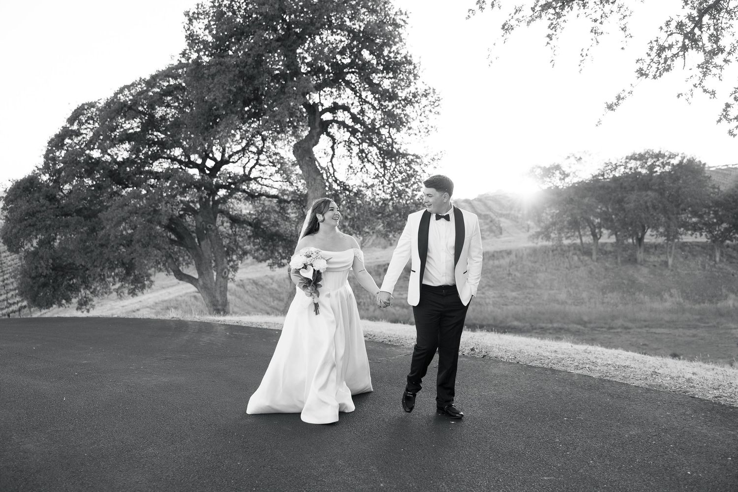 Bride and groom holding hands walking on a scenic road surrounded by trees on their wedding day.
