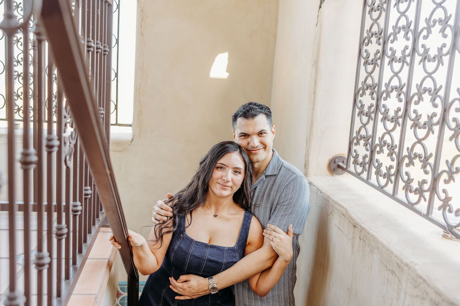 A couple sharing an intimate moment on a staircase with decorative iron railings.