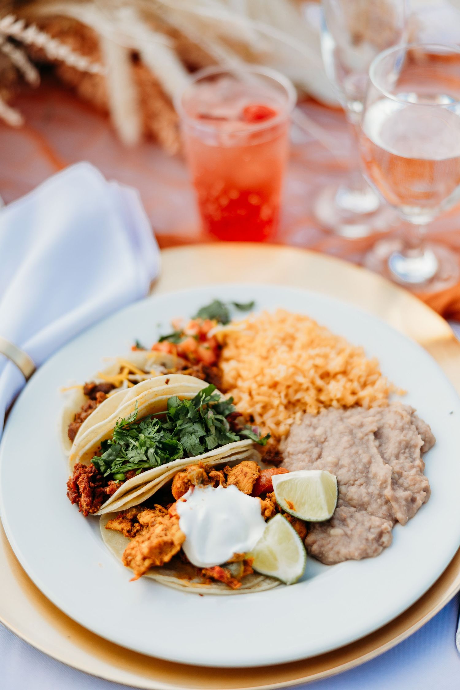 Mexican-style dinner plate with tacos, rice, and beans served with colorful cocktails.