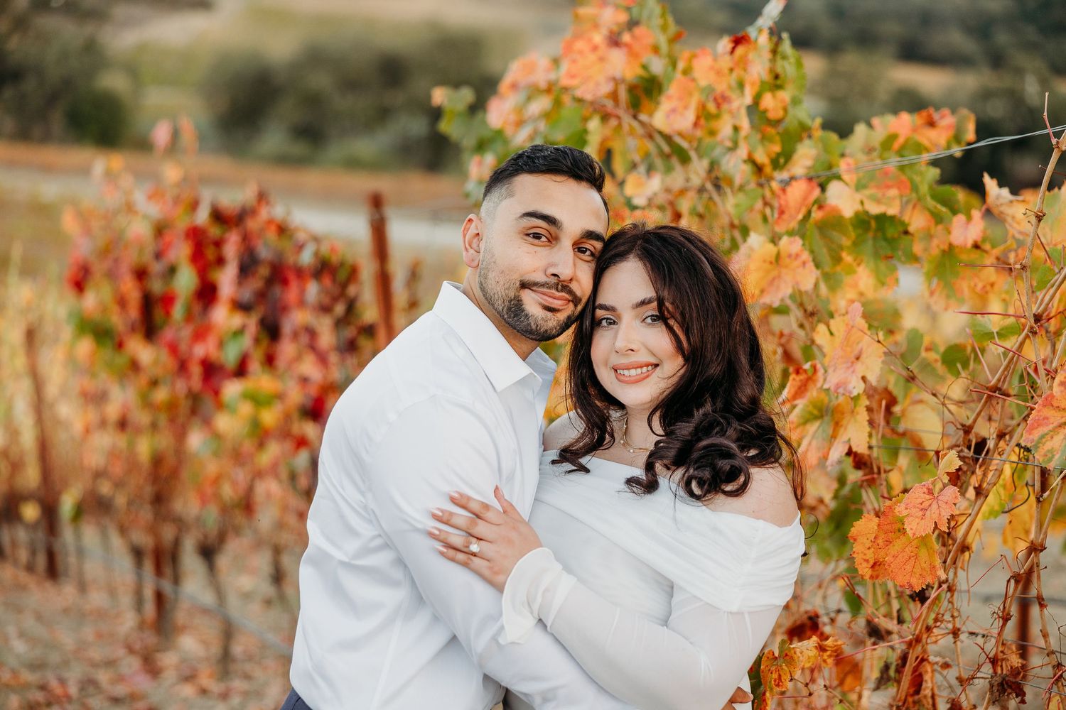 Romantic autumn engagement photos among colorful vineyard vines at sunset.
