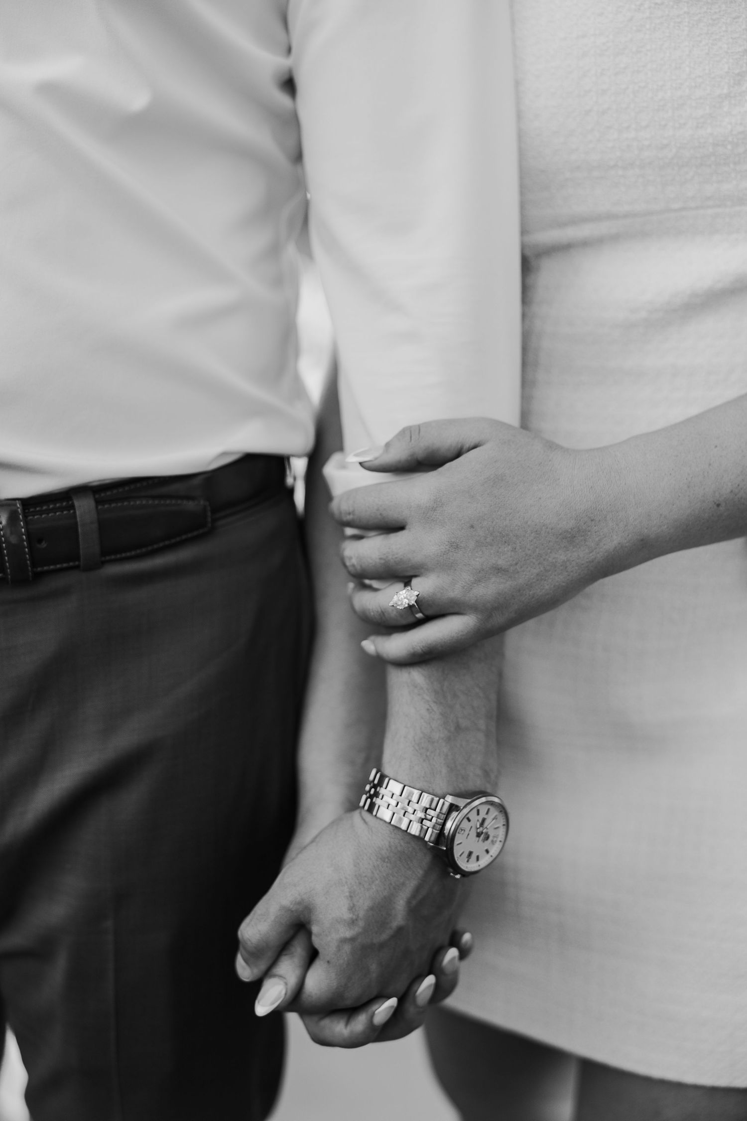 Close-up detail shot of couple's hands and engagement ring against white background.