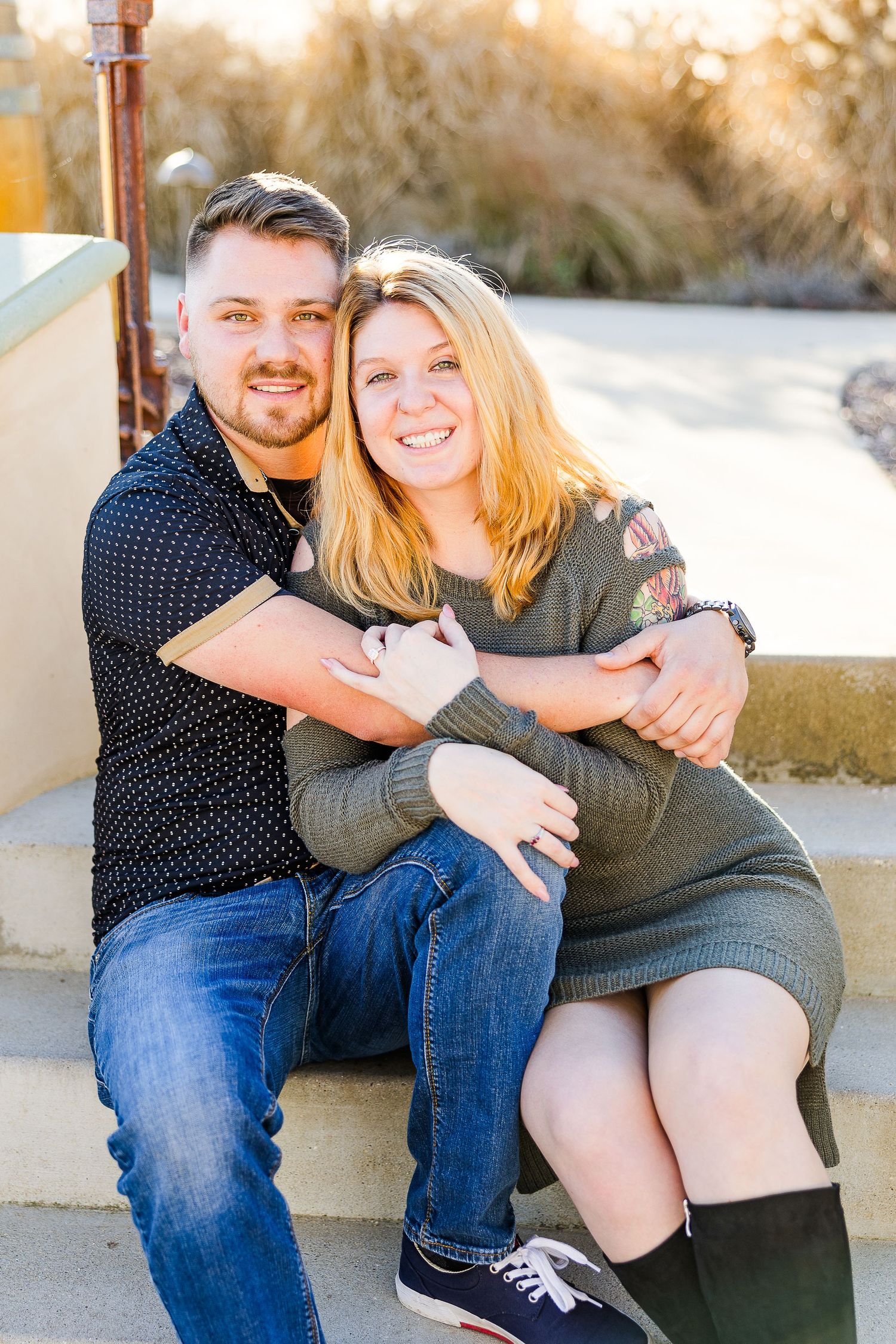 A happy couple poses together on outdoor steps during a sunny afternoon.