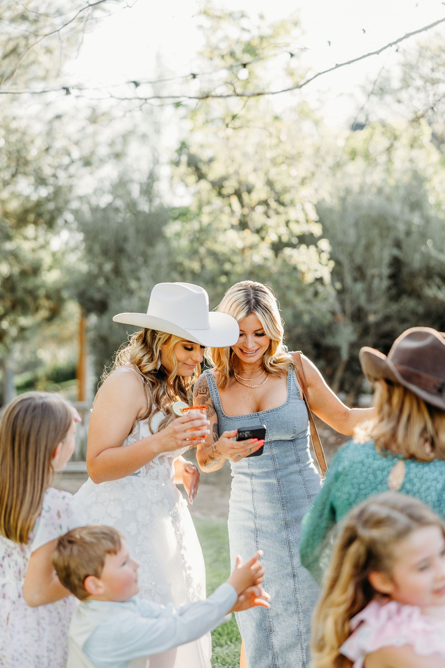 Wedding party enjoying candid moment outdoors wearing cowboy hats and light summer attire.