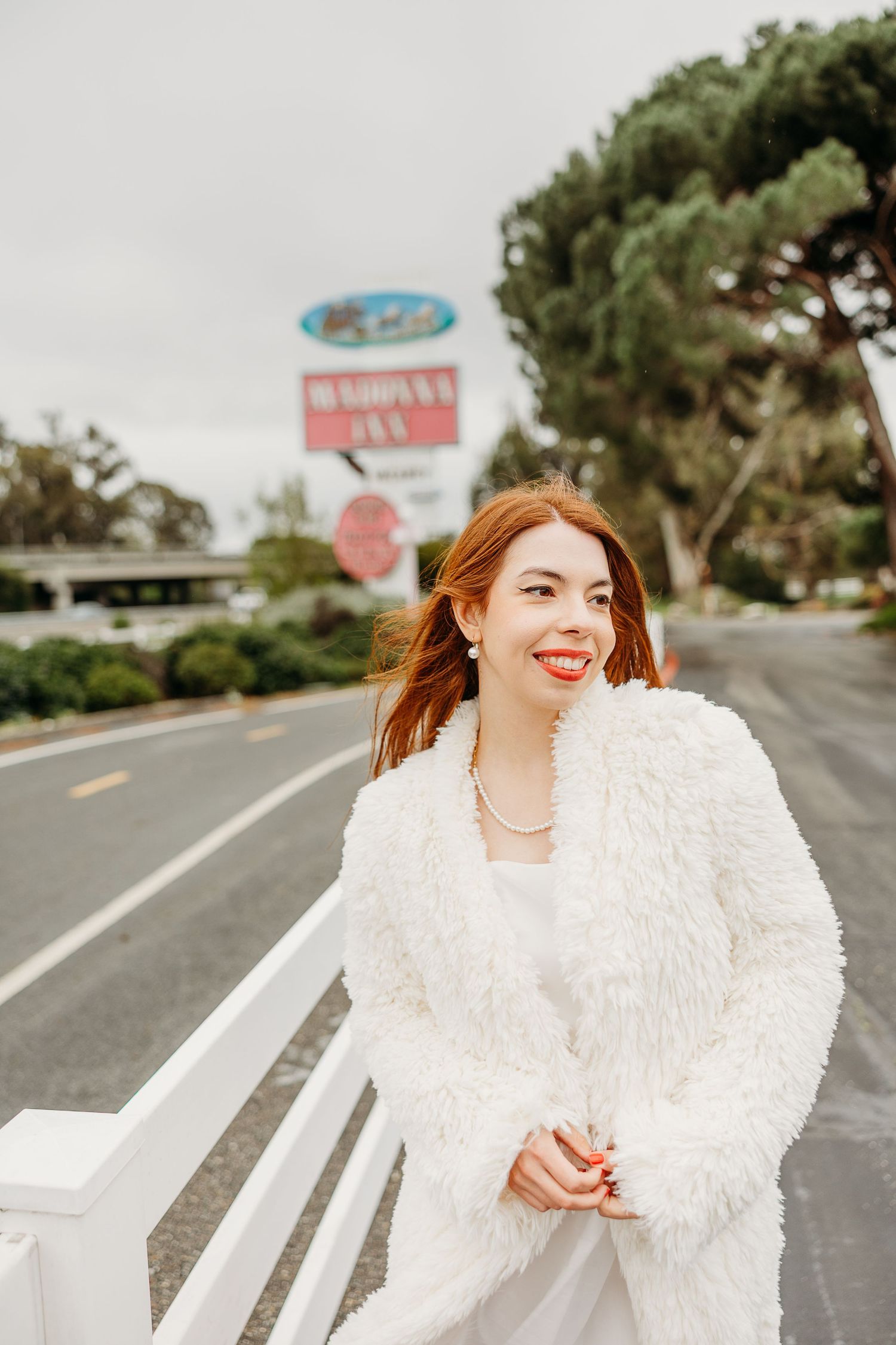 Someone in a fluffy white coat poses confidently on a sunny road with stop signs visible in the distance.