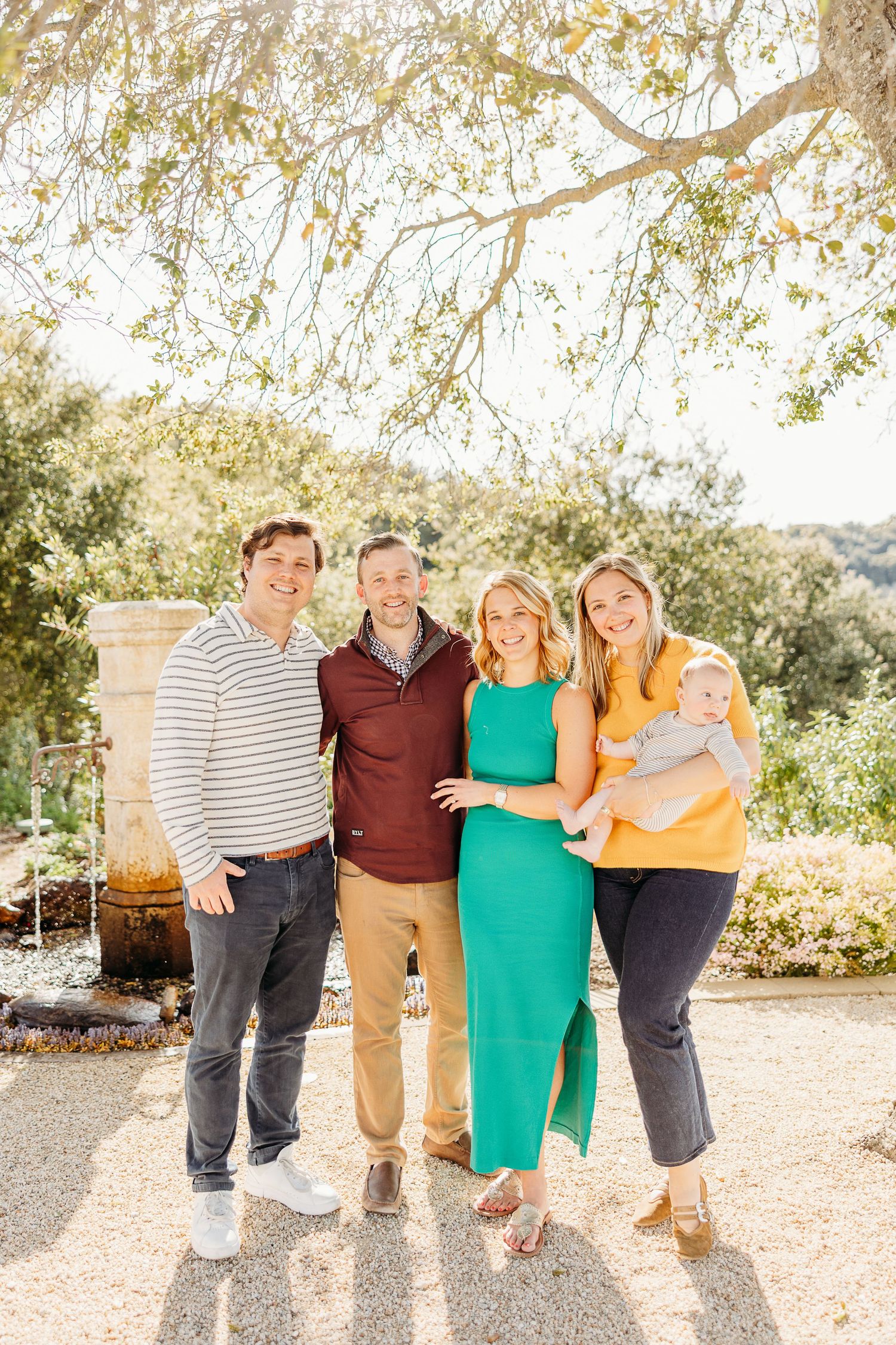 Group enjoying outdoor photo session in coordinating outfits of teal, burgundy, yellow and stripes against natural backdrop.