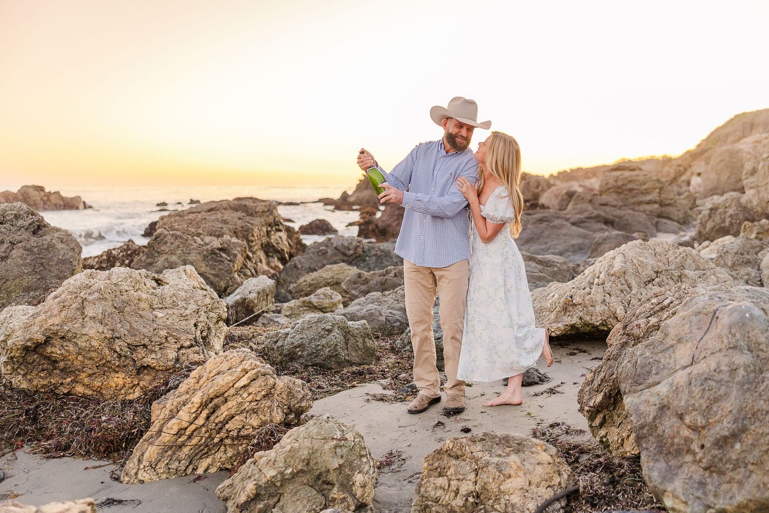 A couple explores rocky coastal formations during a golden sunset photoshoot.