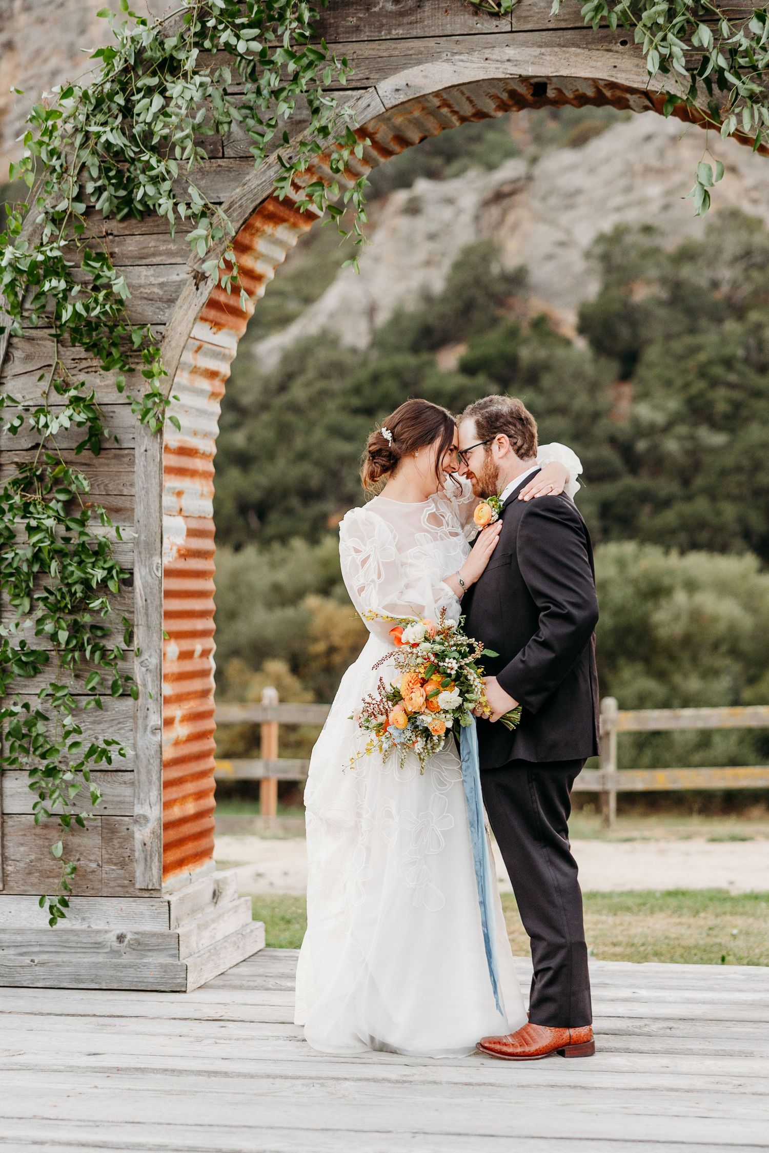 Wedding couple sharing an intimate moment under a rustic brick archway adorned with greenery by the best SLO wedding photographer.