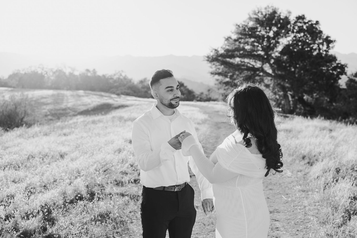 Romantic black and white photo series of a couple embracing and laughing together in a sunny meadow.