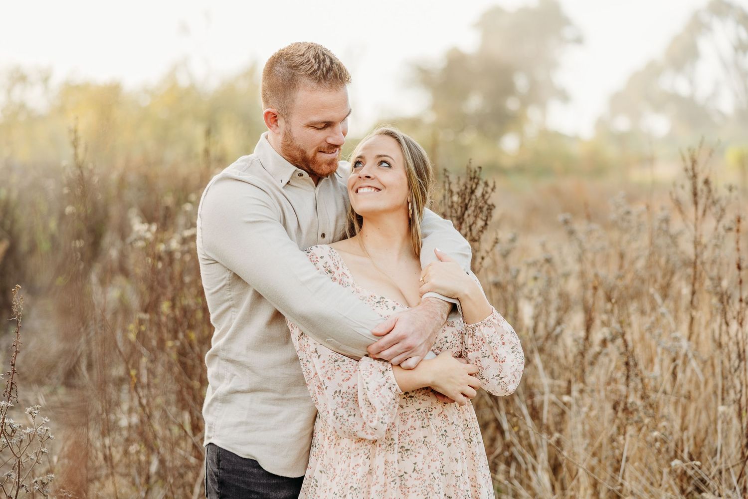 Romantic couple embracing in tall dry grass field during golden hour.