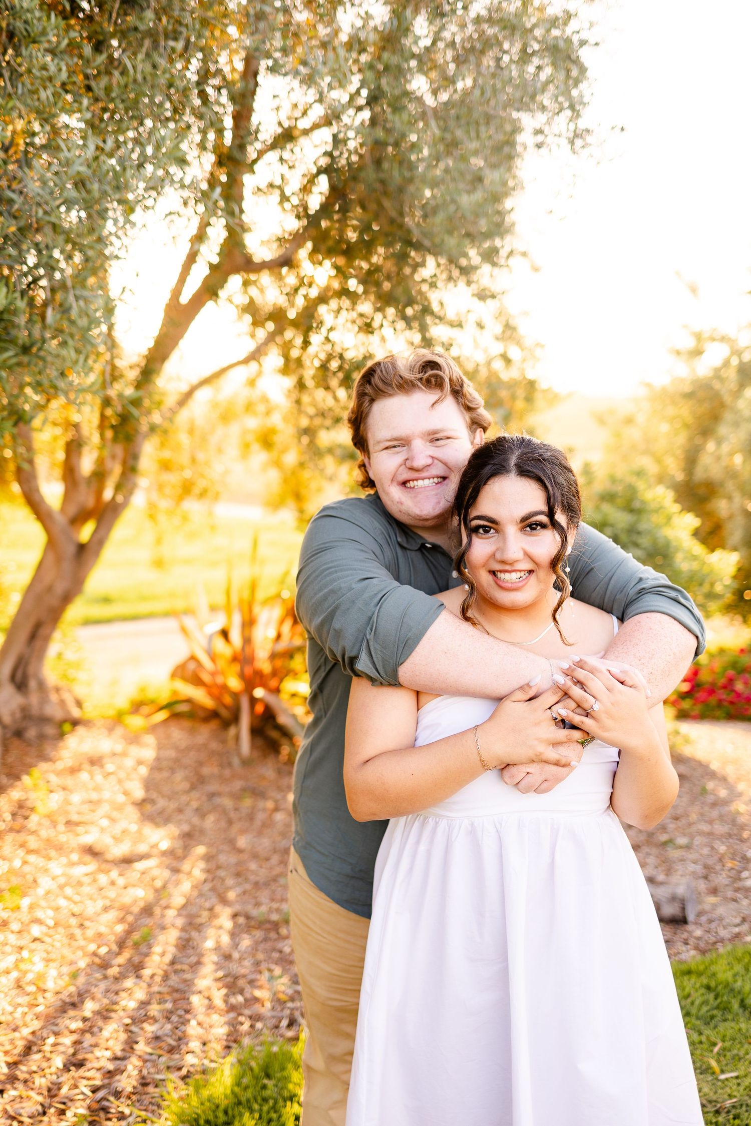 A happy couple embraces while posing for photos in a sun-drenched garden.