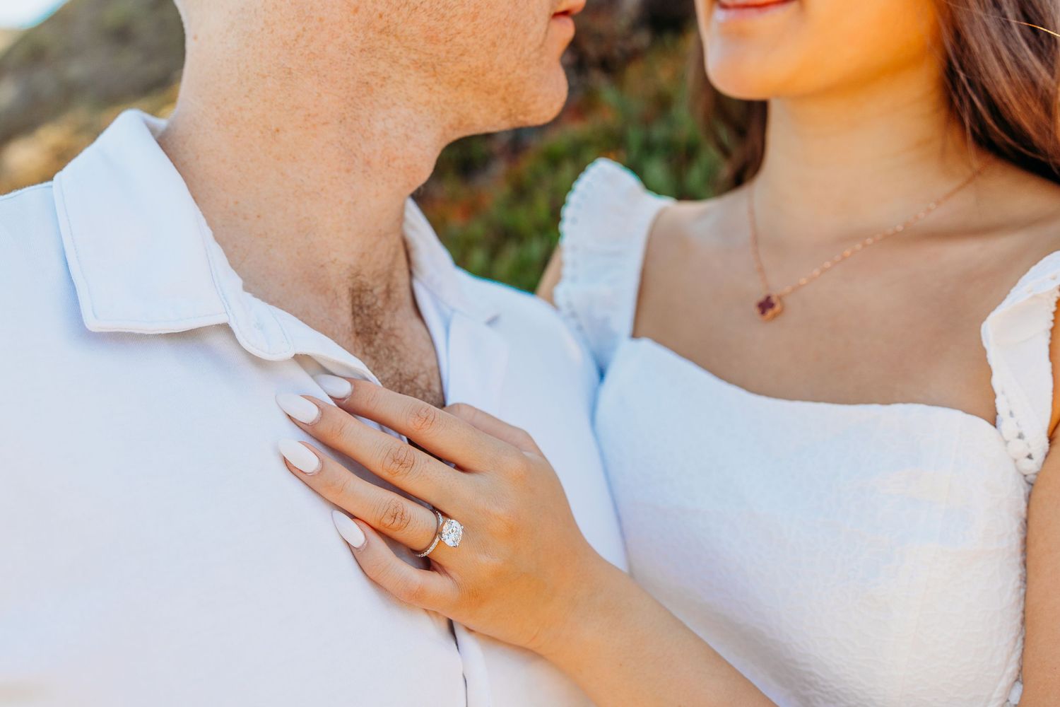 Close-up shot of an engagement ring moment with white attire against natural scenery.