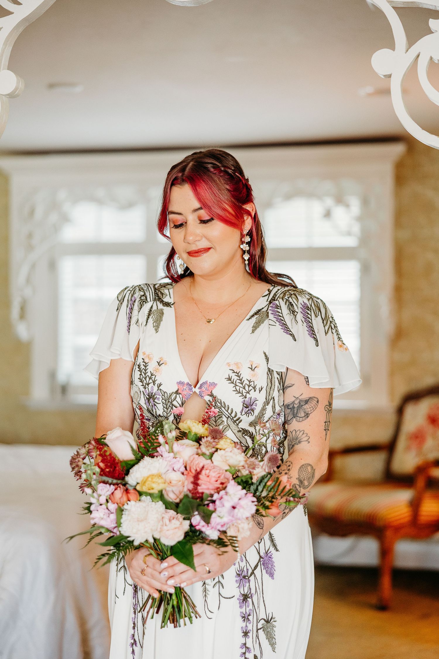 Bride in white dress holding beautiful pink and coral floral bouquet at indoor venue.