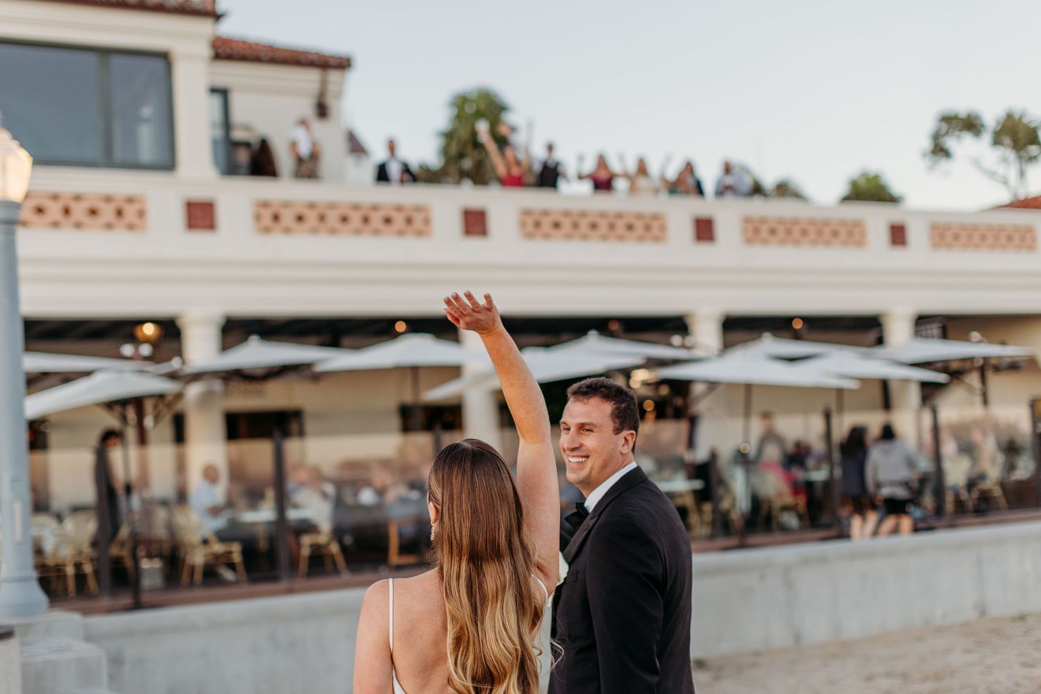 Wedding couple celebrates outside Spanish-style venue with palm trees.
