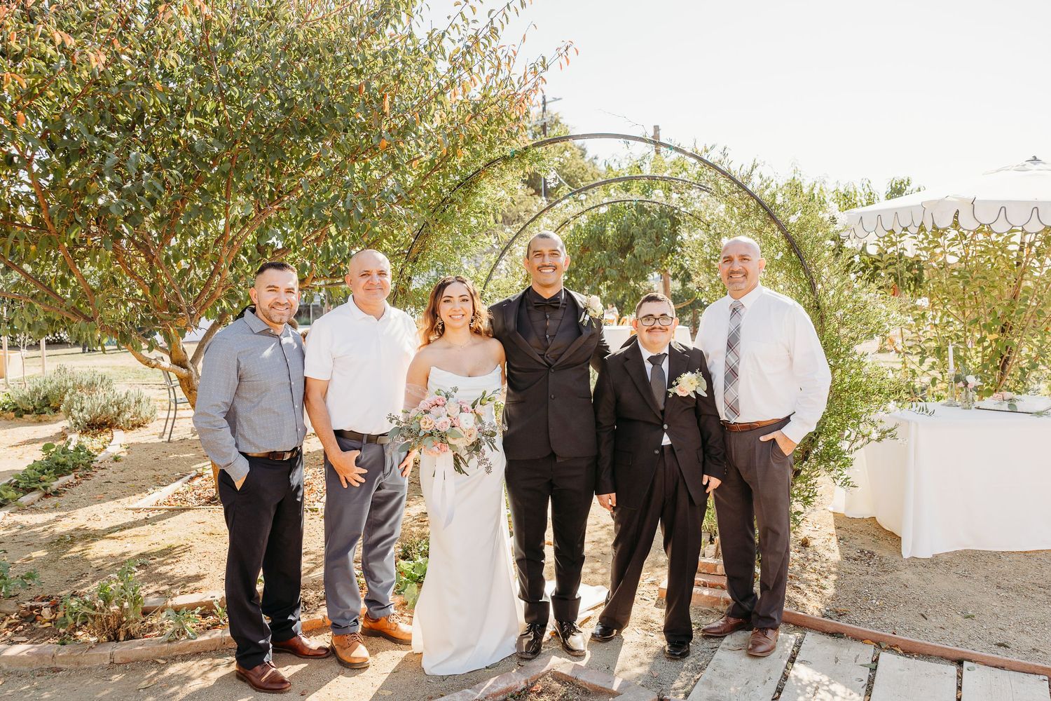Wedding party gathered outdoors in natural lighting against a scenic backdrop.