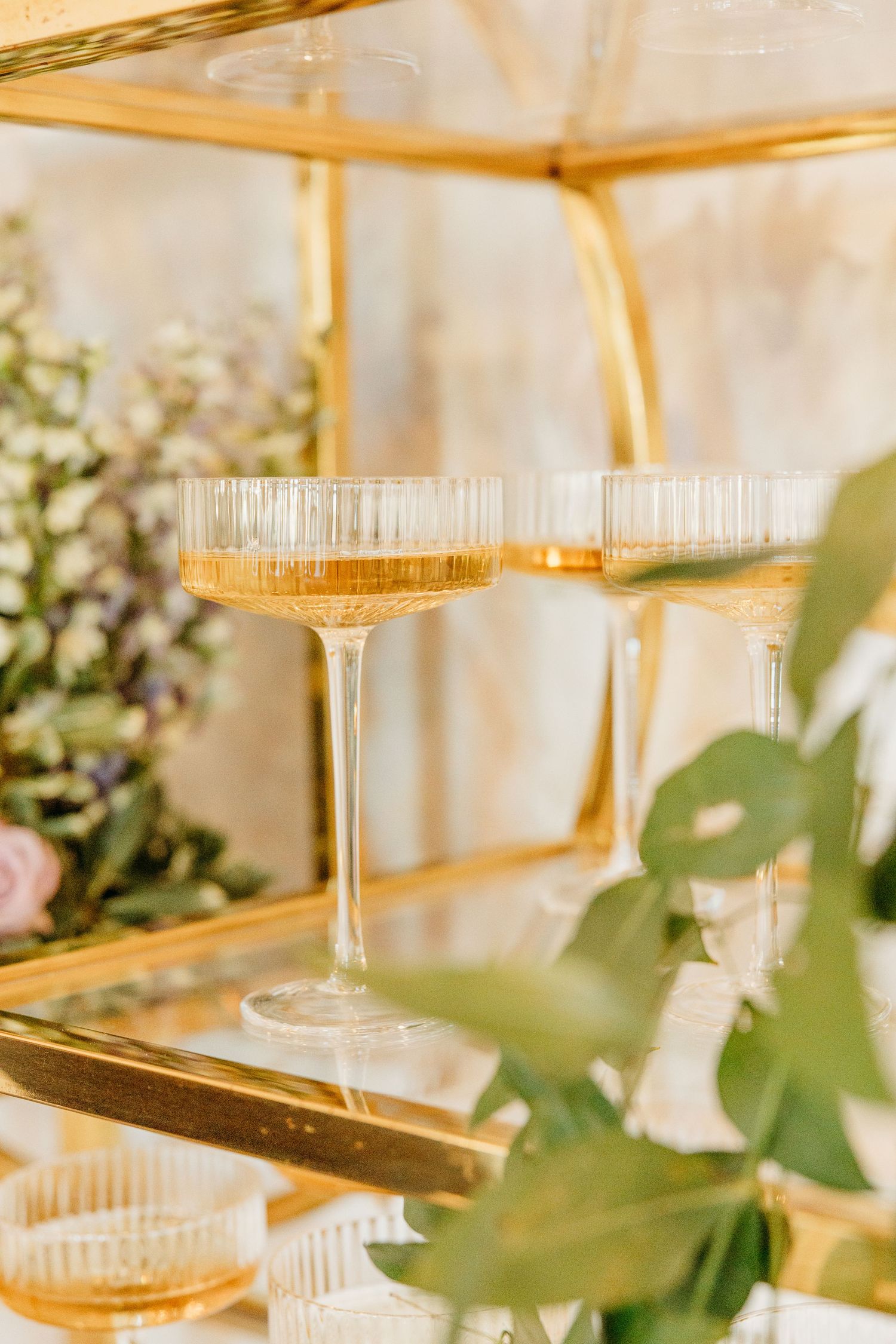Elegant champagne glasses with gold-rimmed edges sit on a table with soft greenery in the background.