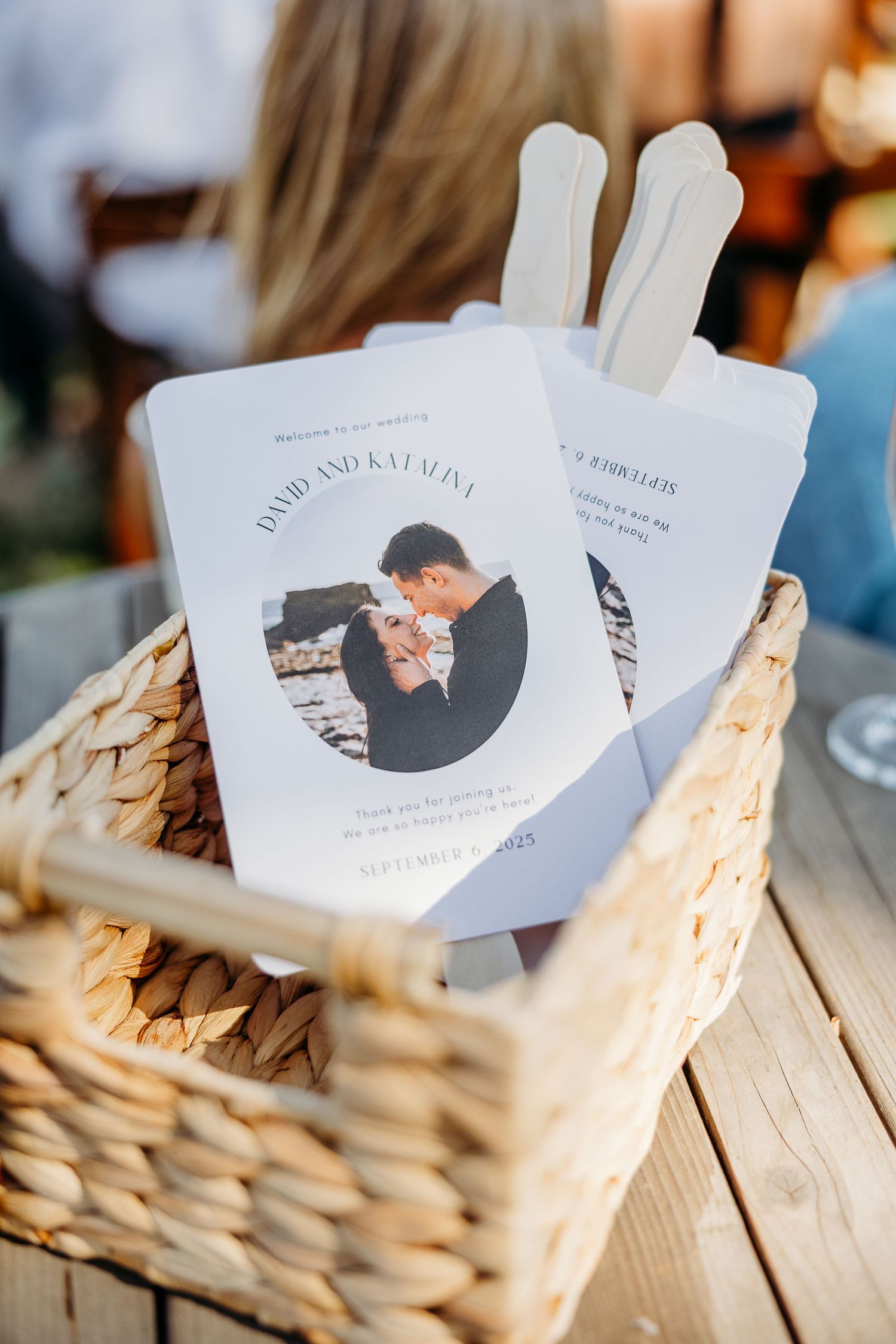 Custom printed paper popsicle stick fan wedding favors displayed on a rustic wooden surface at a reception.