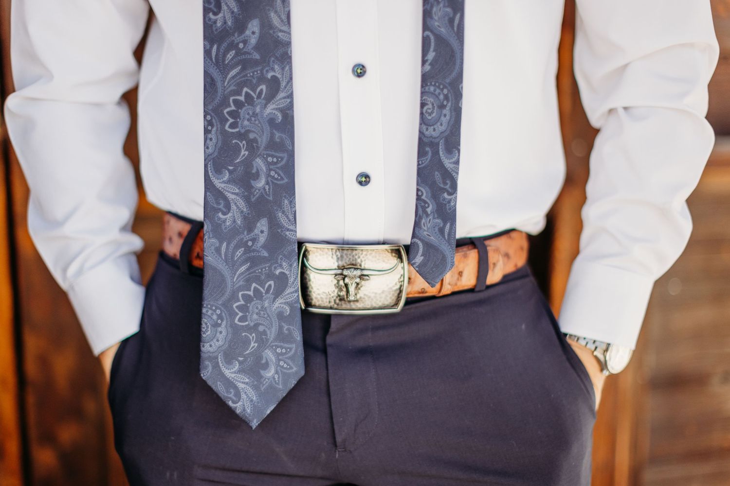Close up of formal attire showing gray patterned tie and western-style belt buckle.
