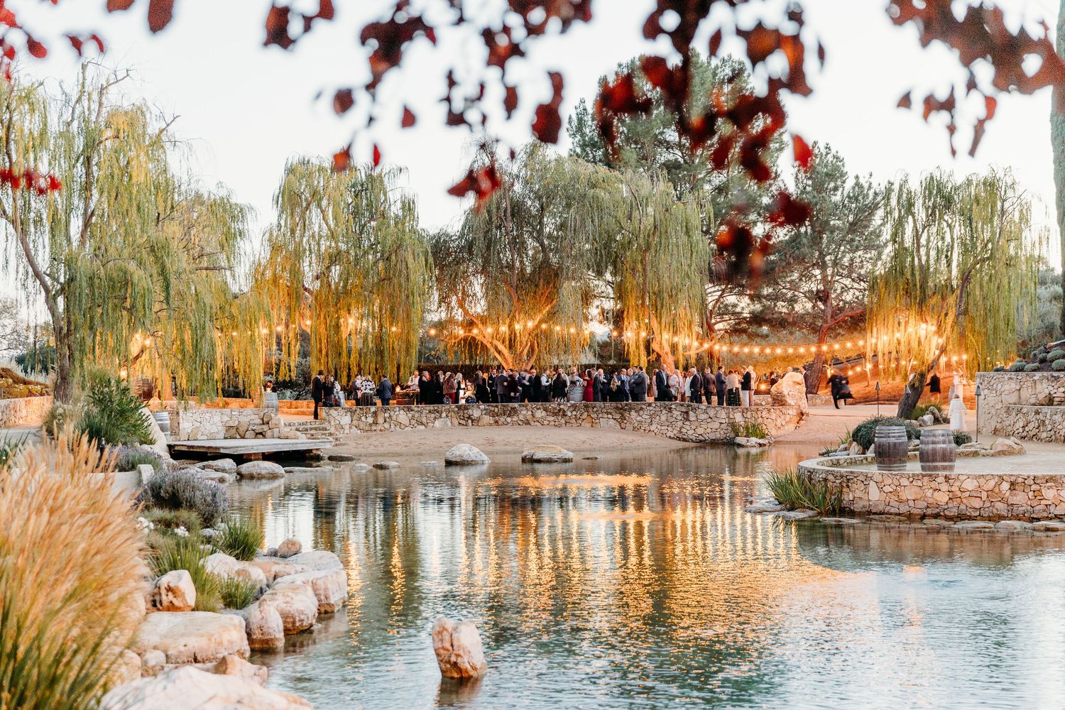 Outdoor wedding venue with string lights and water features at sunset.