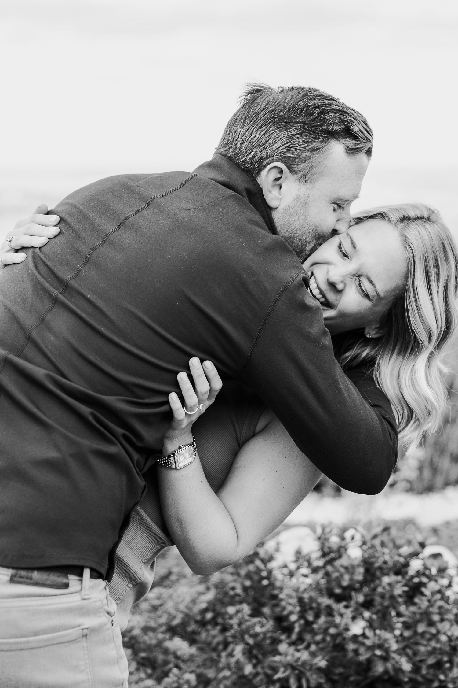A couple shares a passionate kiss while standing near shrubbery as seen in a series of black and white romantic photos.