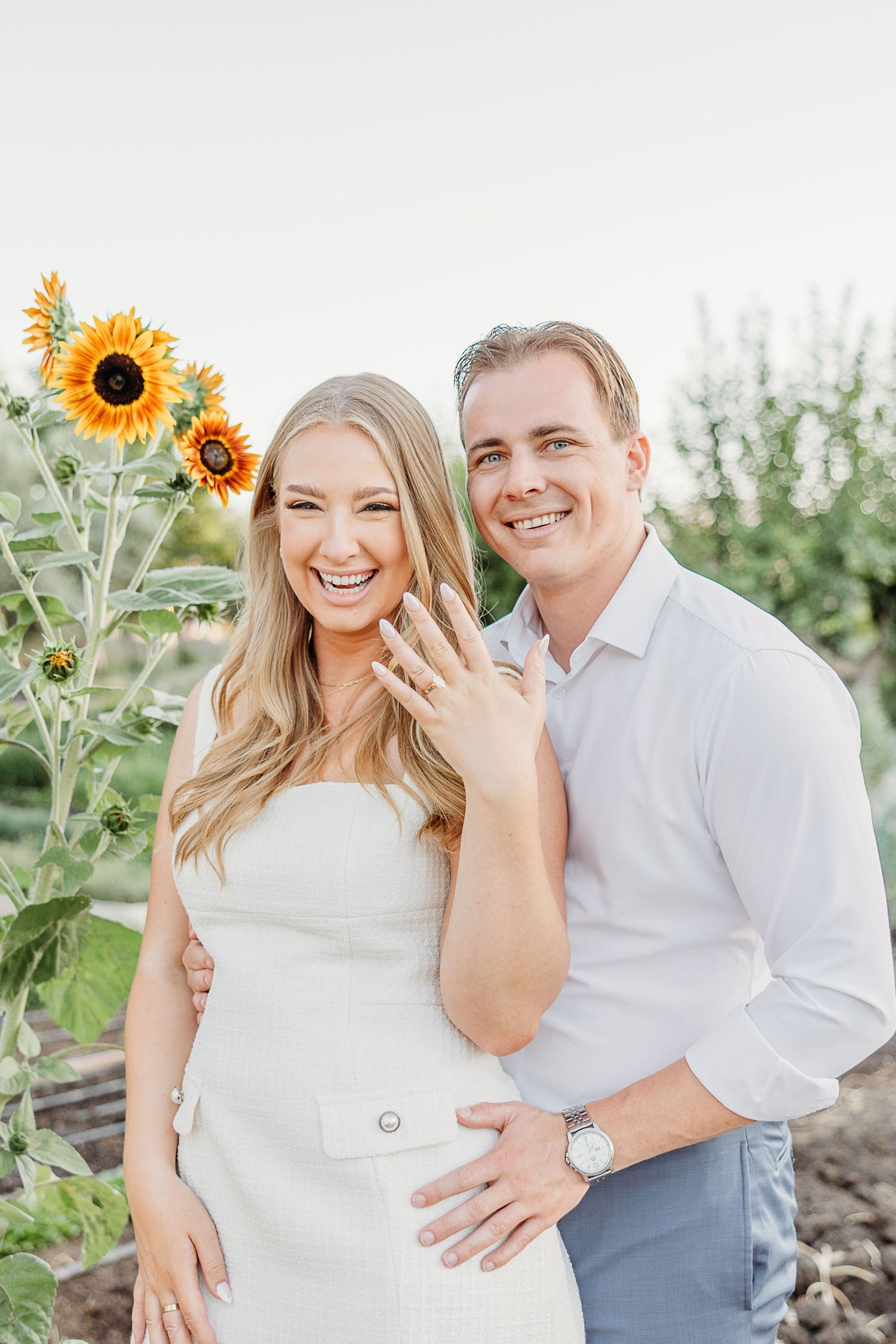 Couple poses together in sunflower field during maternity photoshoot wearing white and blue casual attire.