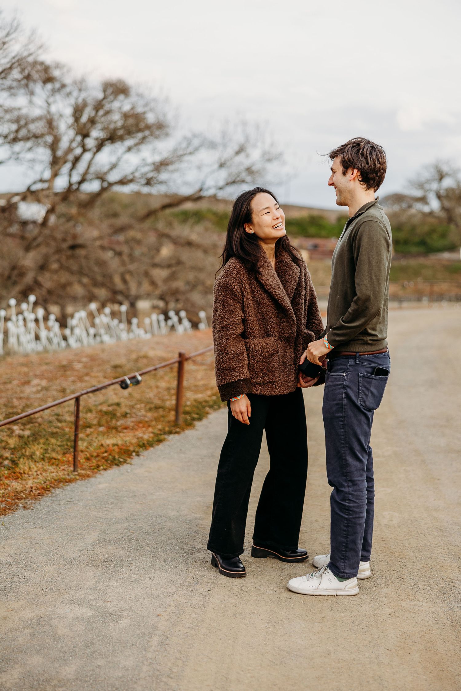 A couple shares a joyful moment while walking together on a gravel path during autumn.