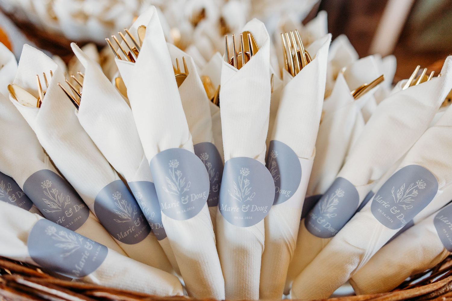 Wooden utensils wrapped in white napkins with gray monogrammed seals arranged in a woven basket.