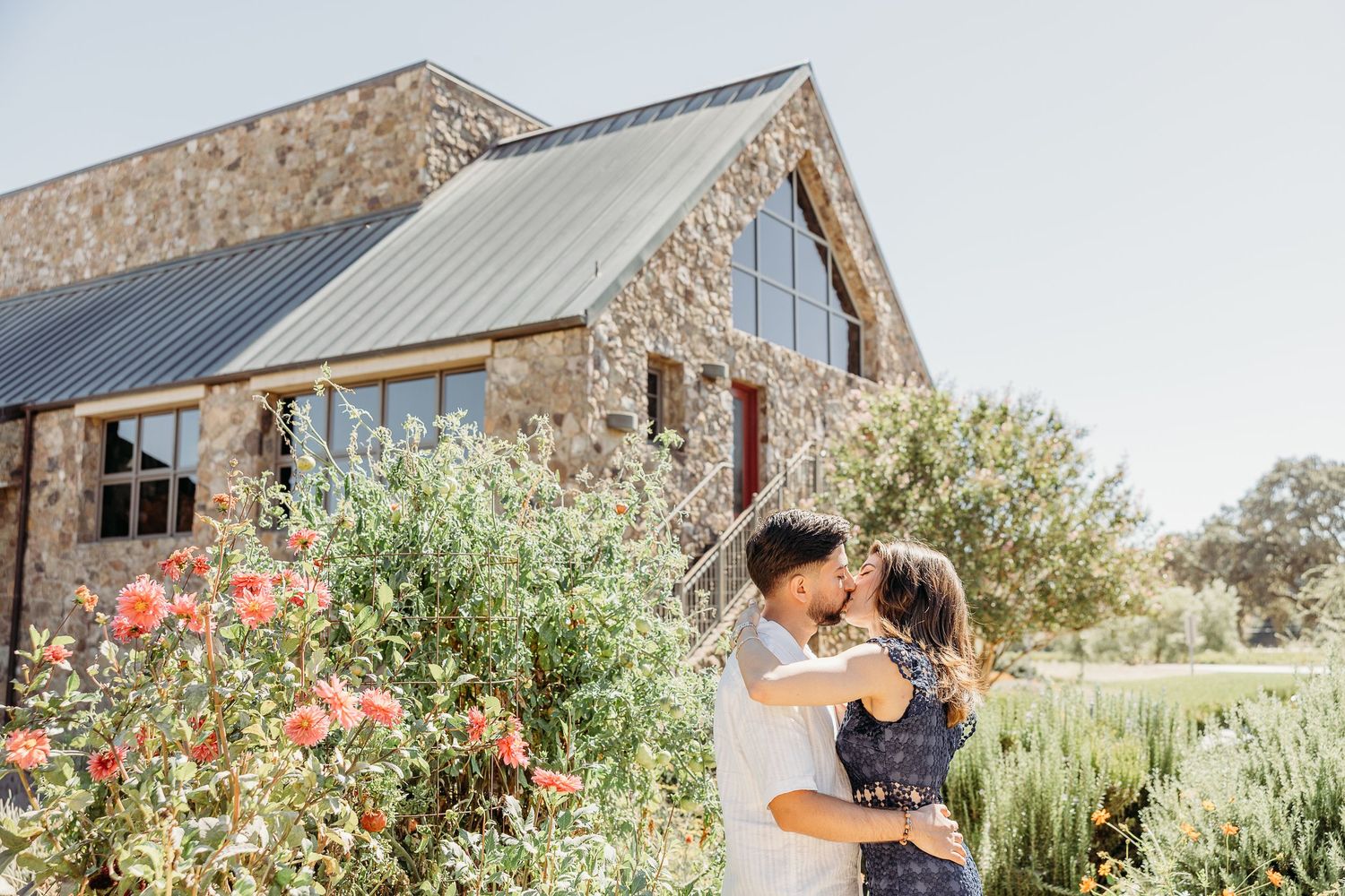Stone winery building with modern architecture and landscaped gardens under blue sky.