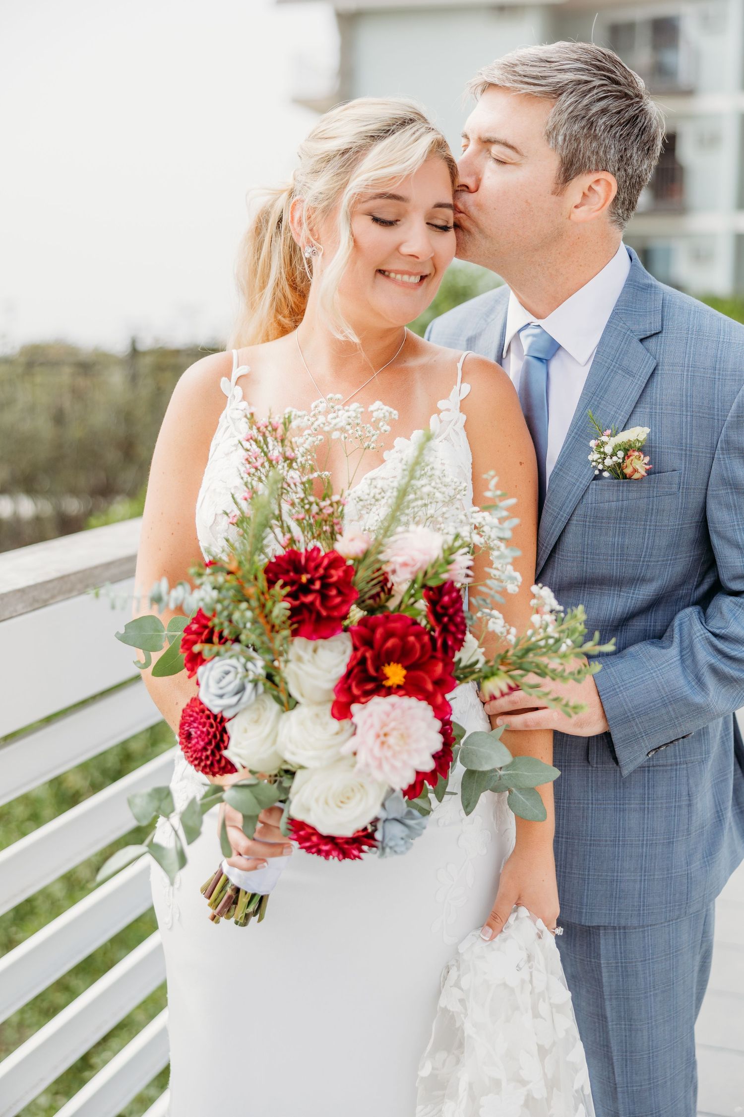 Intimate wedding moment captured on coastal balcony with floral bouquet.