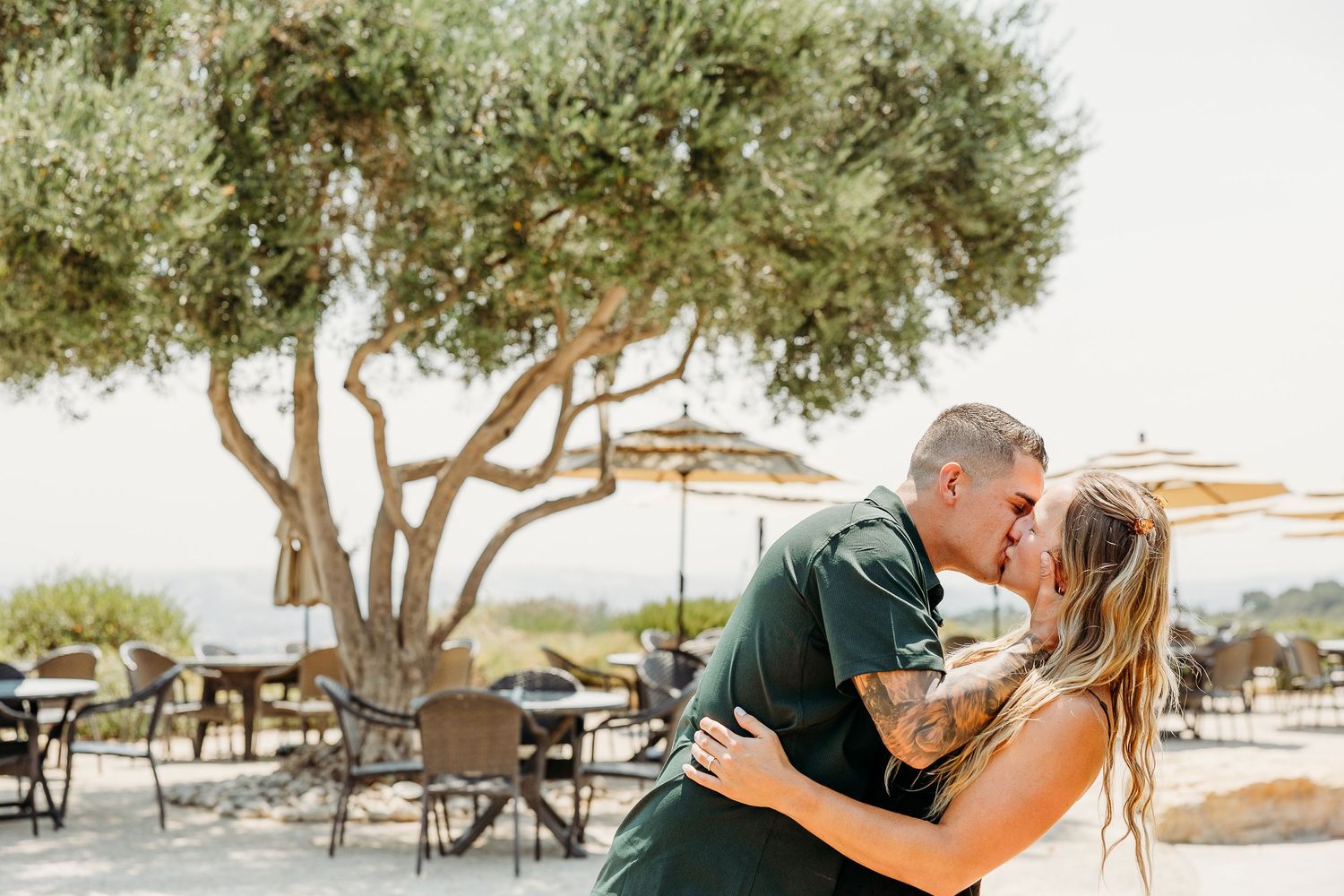 A romantic moment shared on an outdoor patio with olive trees and cafe tables in the background.