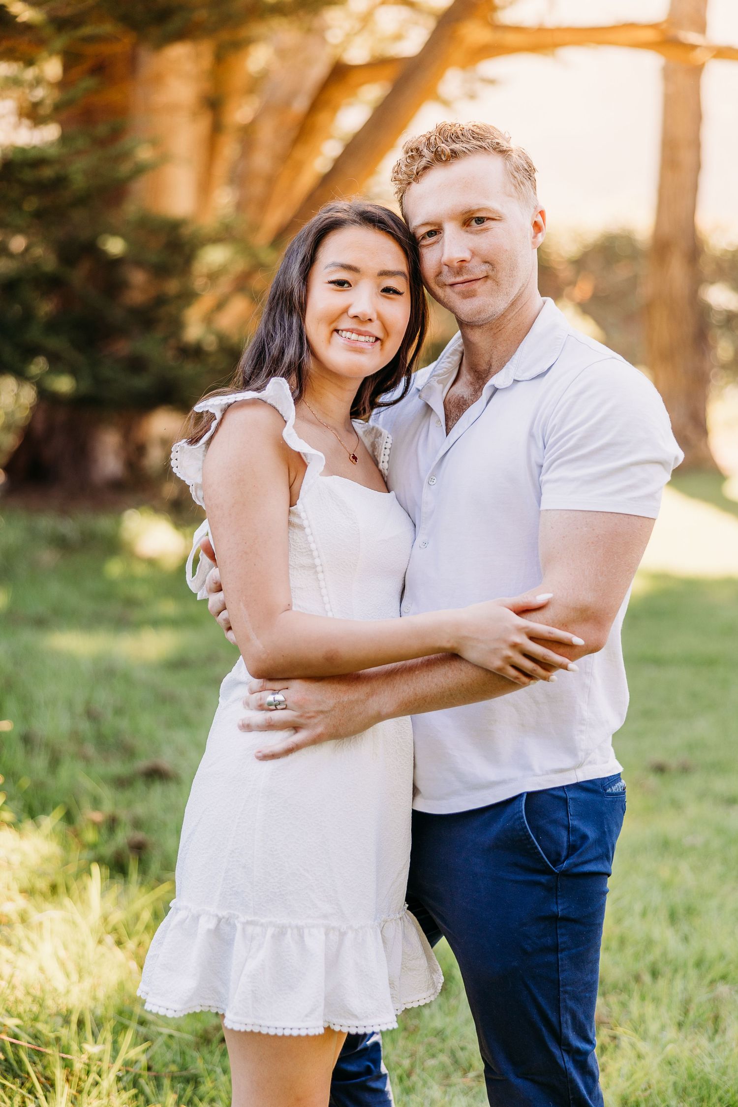 Happy couple in coordinated white outfits pose together in sunny outdoor setting.