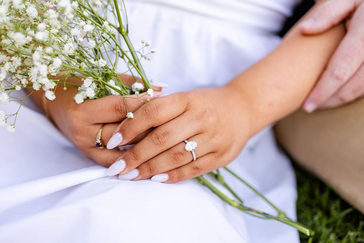 Close up of hands holding baby's breath flowers with engagement ring.