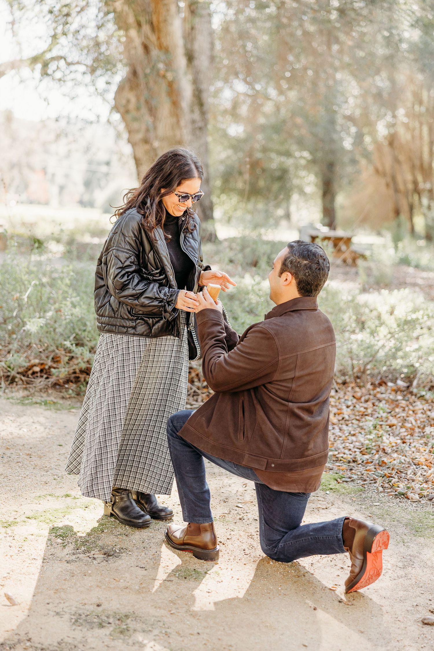 A couple shares a tender moment in a forest setting while taking photos on a fall day.
