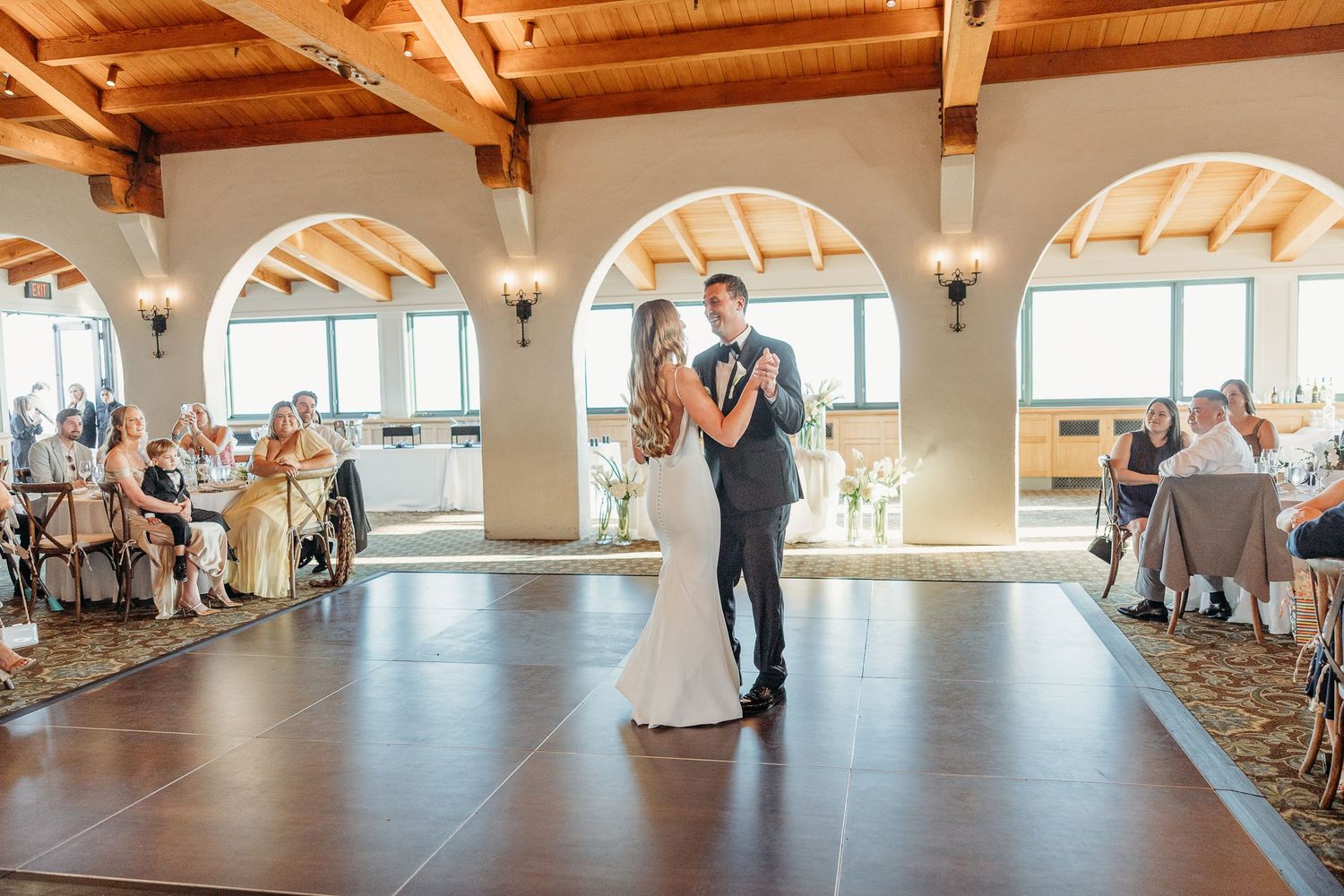 Wedding reception venue with exposed wooden beams and arched windows overlooking a scenic view.