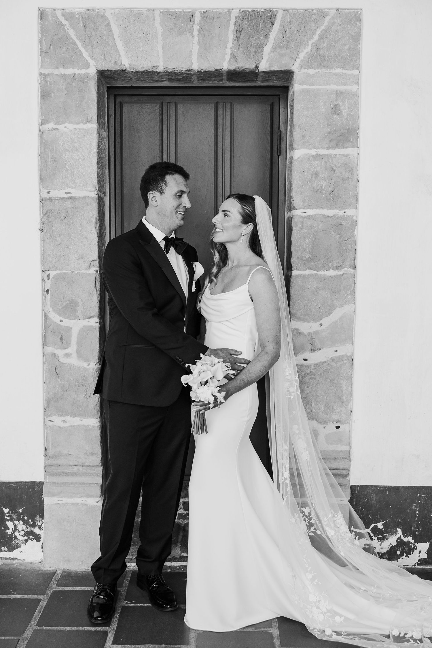 Black and white wedding portraits captured in front of stone wall architecture.