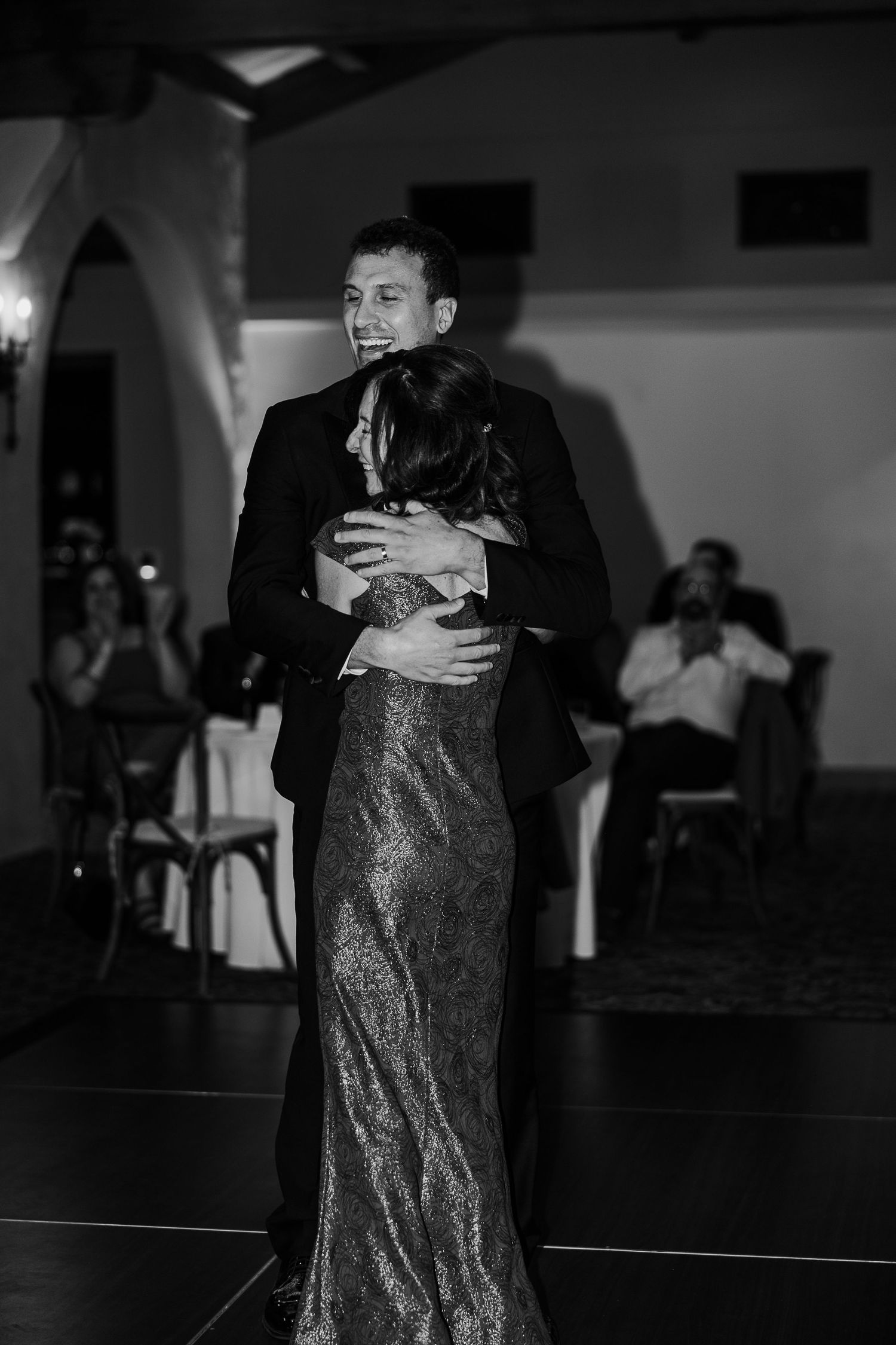 Couples slow dancing in formal attire on a dimly lit ballroom floor during evening reception.