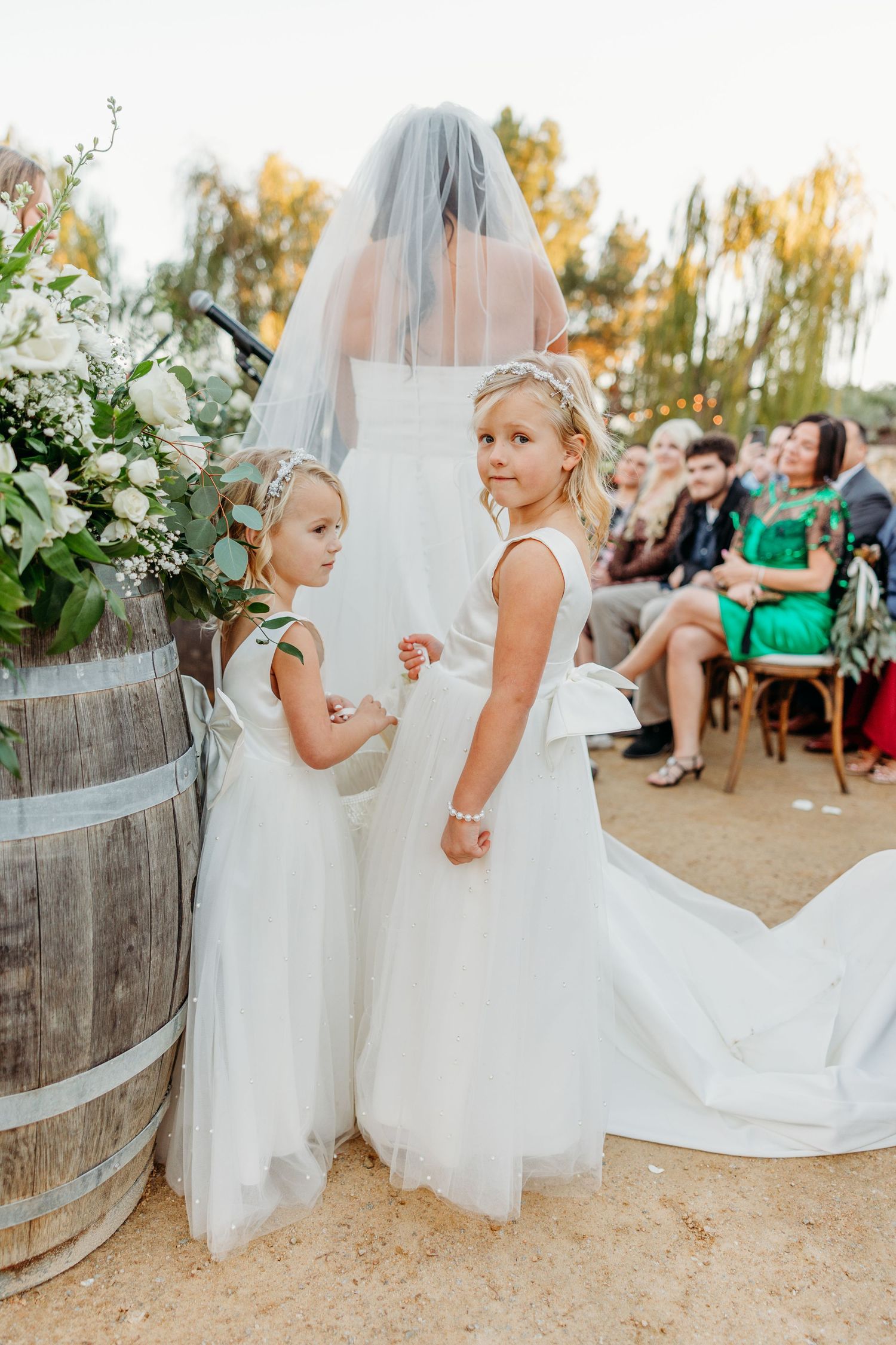 Young attendants in white dresses walking along a sandy outdoor venue path.