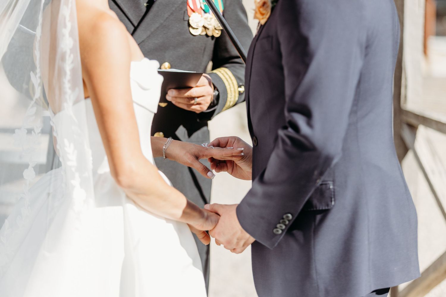 A couple in wedding attire walks together while holding hands and smiling during their outdoor ceremony.