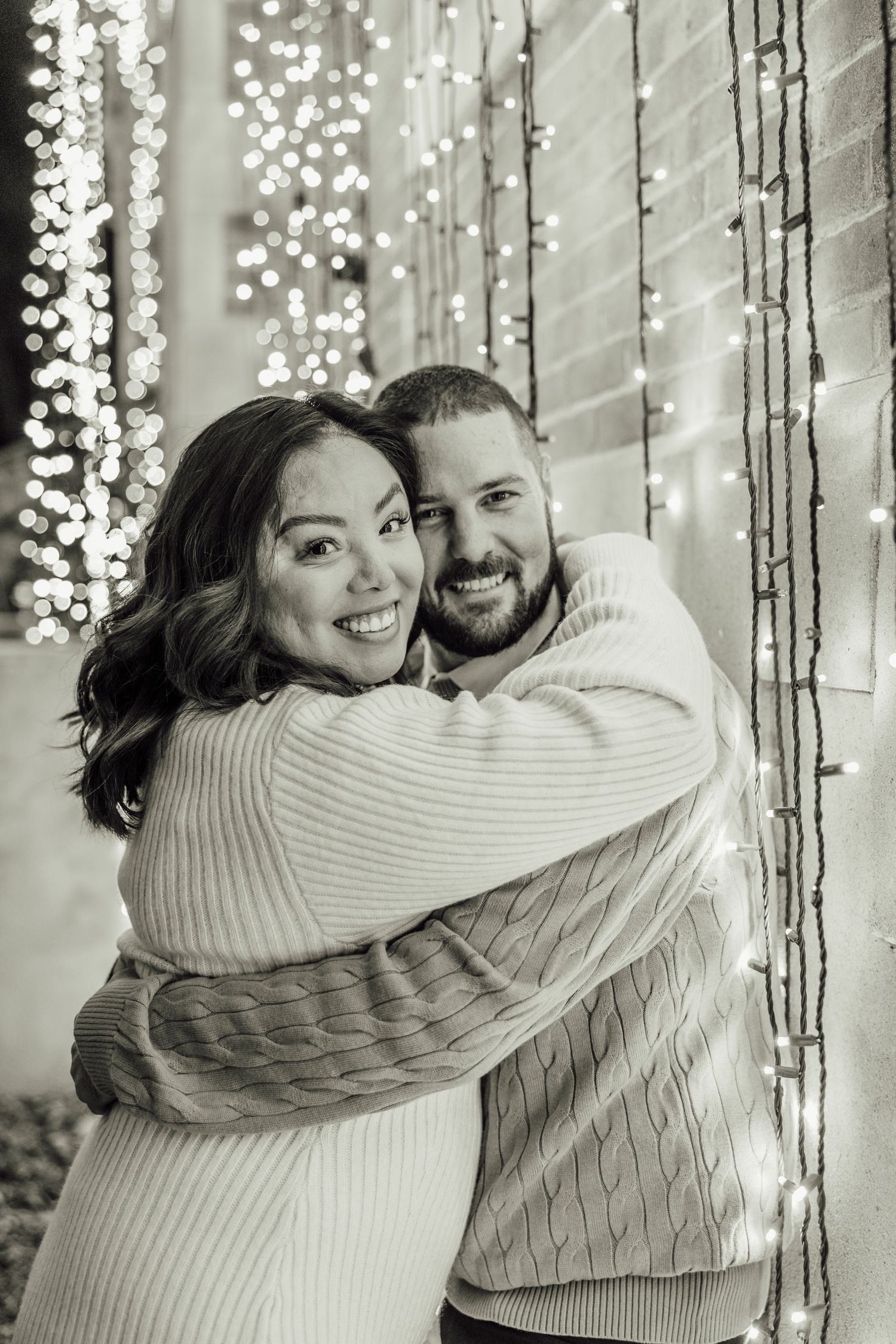 Black and white portrait of a couple embracing under string lights creating a romantic atmosphere.