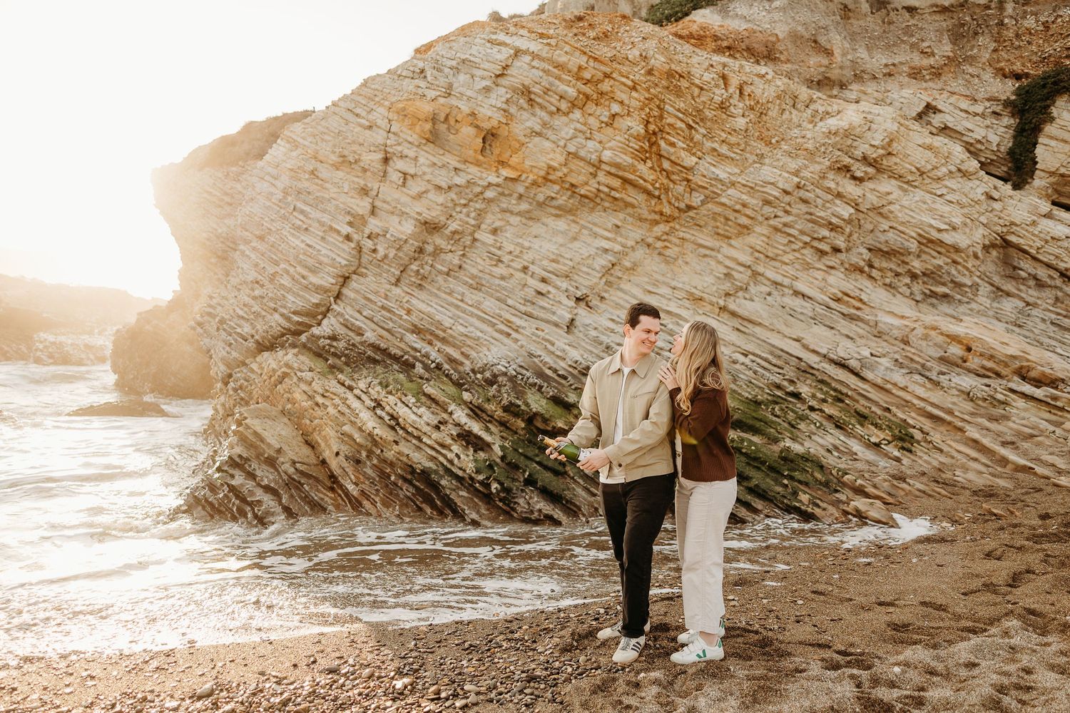 Couple walking together along a scenic rocky coastline during sunset.