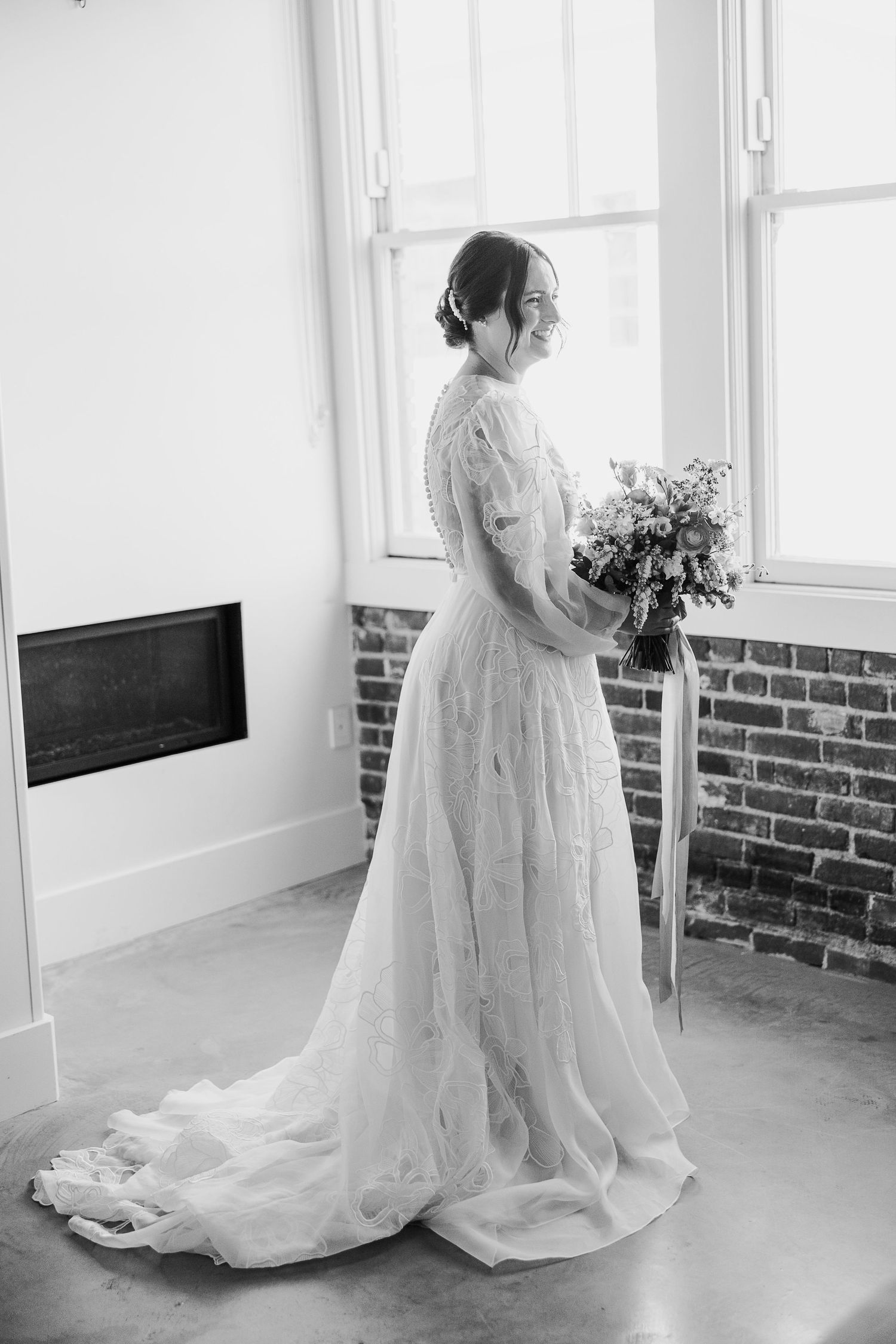 Black and white portrait of bride in lace gown holding bouquet by window of Hotel Cerro SLO.