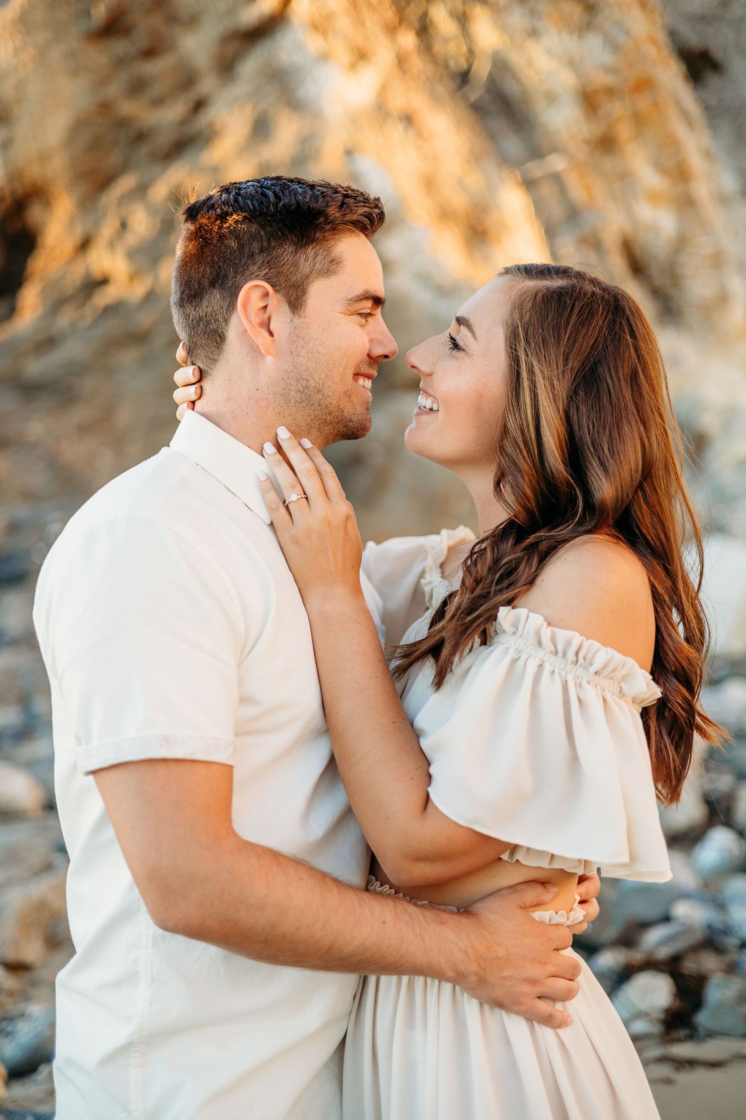 A couple shares an intimate moment against rocky coastal backdrop.